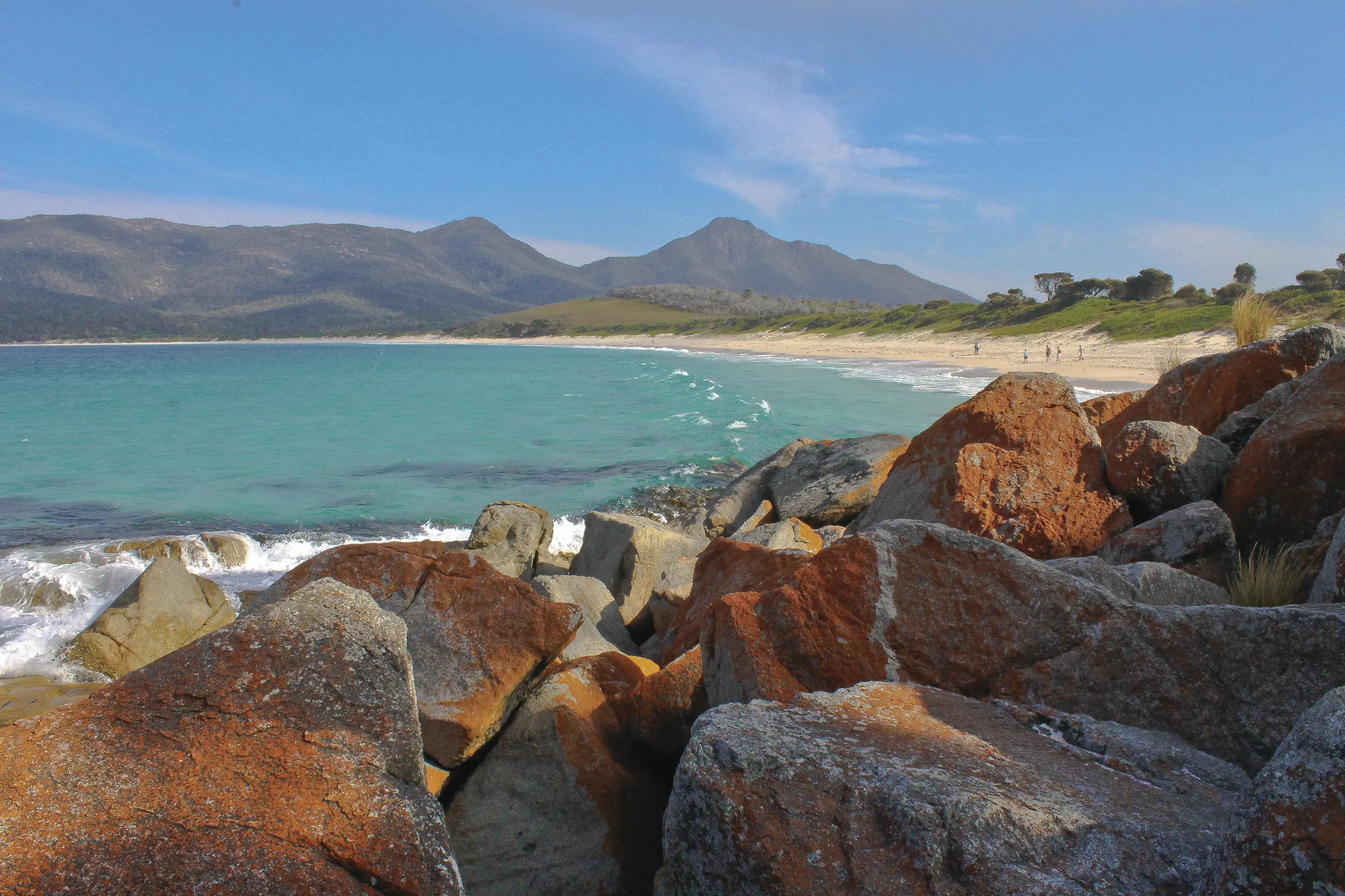 Stanning wide angle image of Wineglass Bay Beach. With striking blue ocean, vibrant stones and lush mountains in the background.