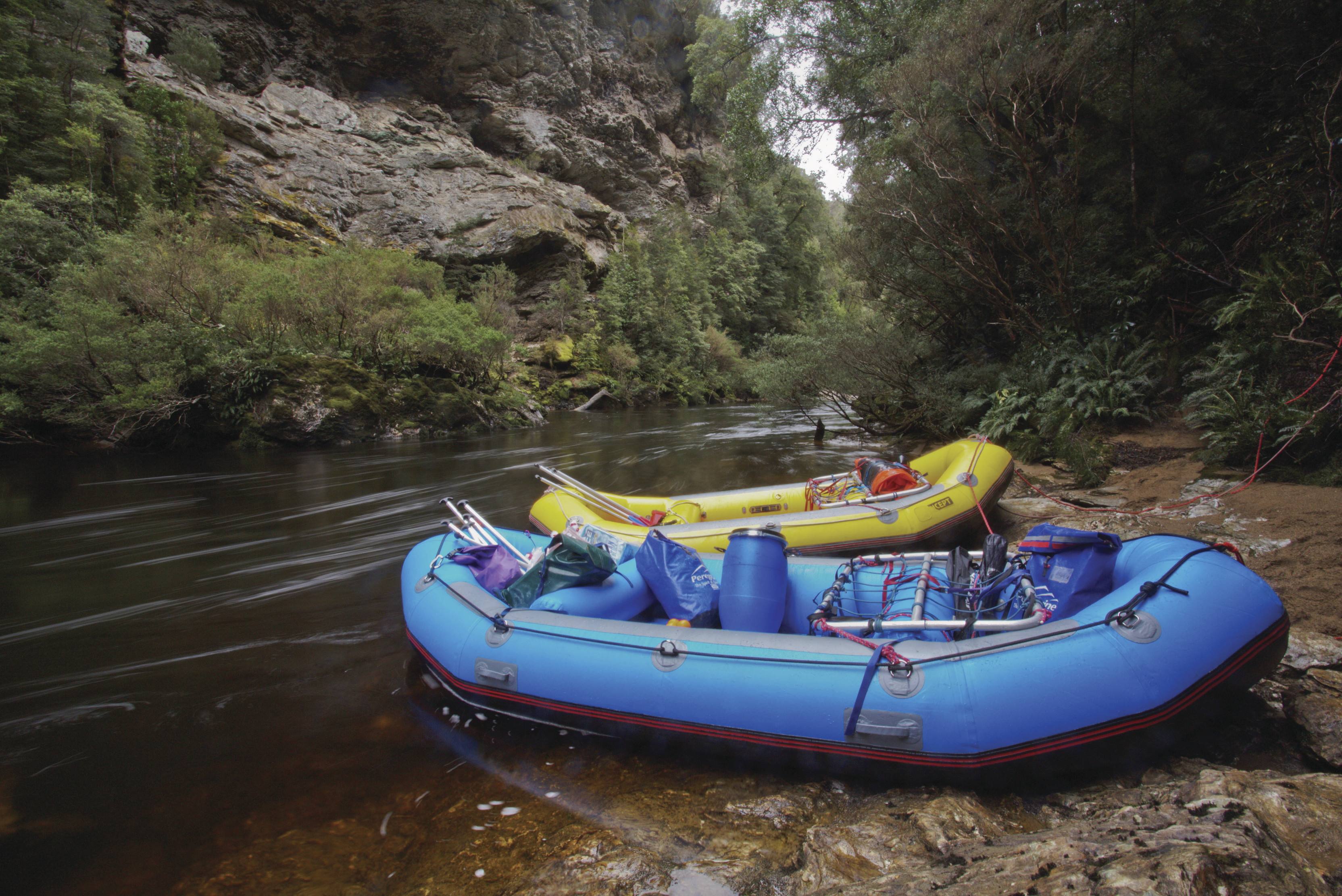 A blue and yellow raft docked in an area of the Franklin River, hosted by Water By Nature Tasmania.