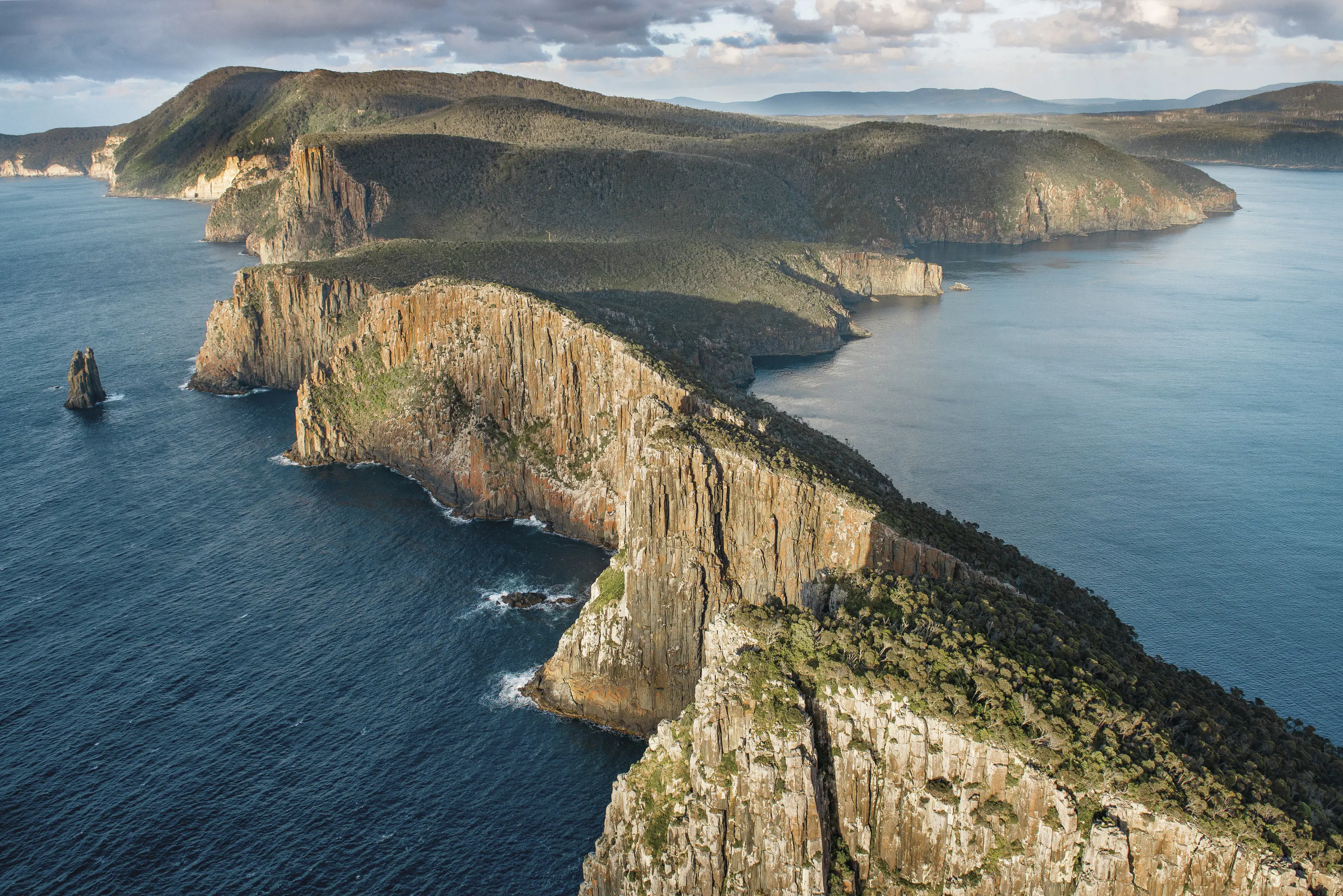 Breathtaking aerial image of the Three Capes Track - Cape Hauy. Top of the cape covered in lush greenery with steep rock cliffs to pristine blue ocean.