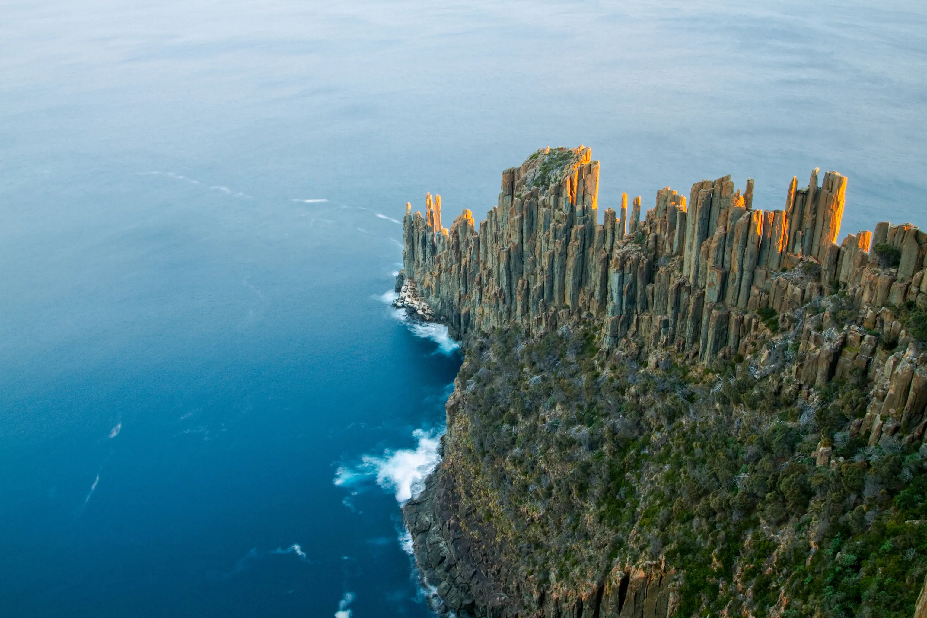 An aerial view looking at a headland jutting out into the sea, made up of distinctive column like rocks. Cape Raoul, Tasman National Park.