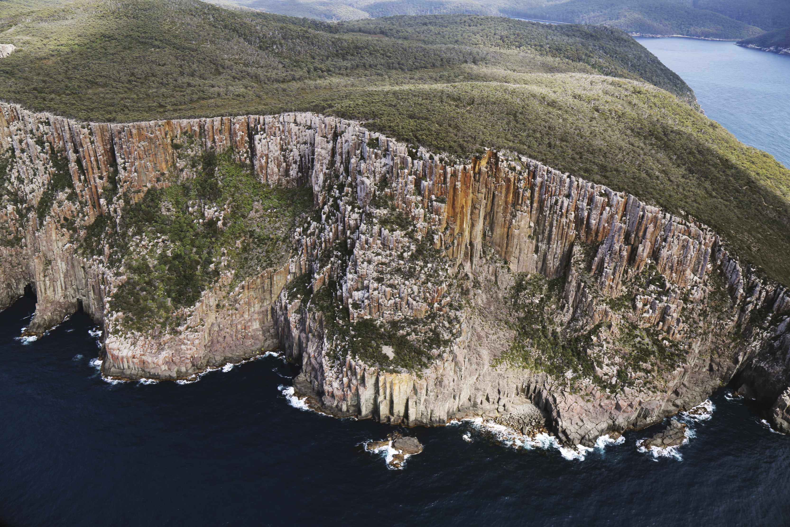 Breathtaking aerial image of the Three Capes Track - Monument Cliffs. Top covered in lush greenery with the steep the cliffs to deep blue ocean.