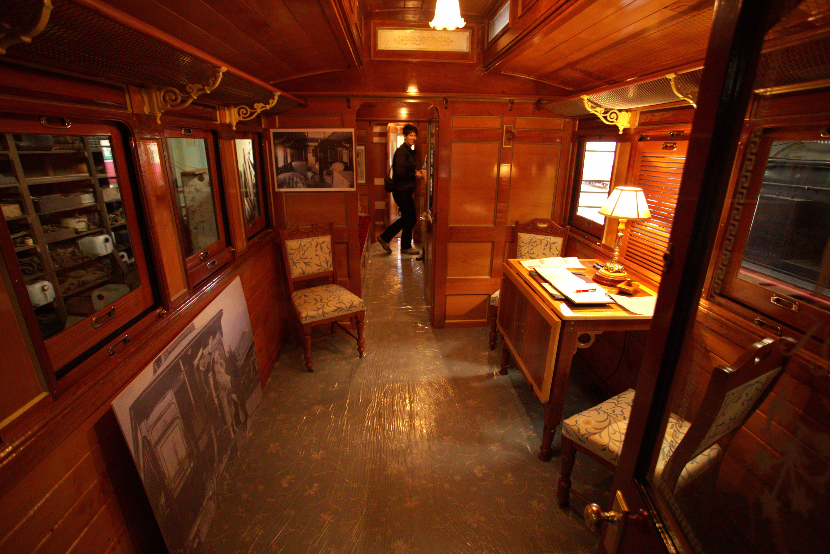Image inside a carriage of a vintage train. With a dark wooden interior filled with vintage furniture and lighting.