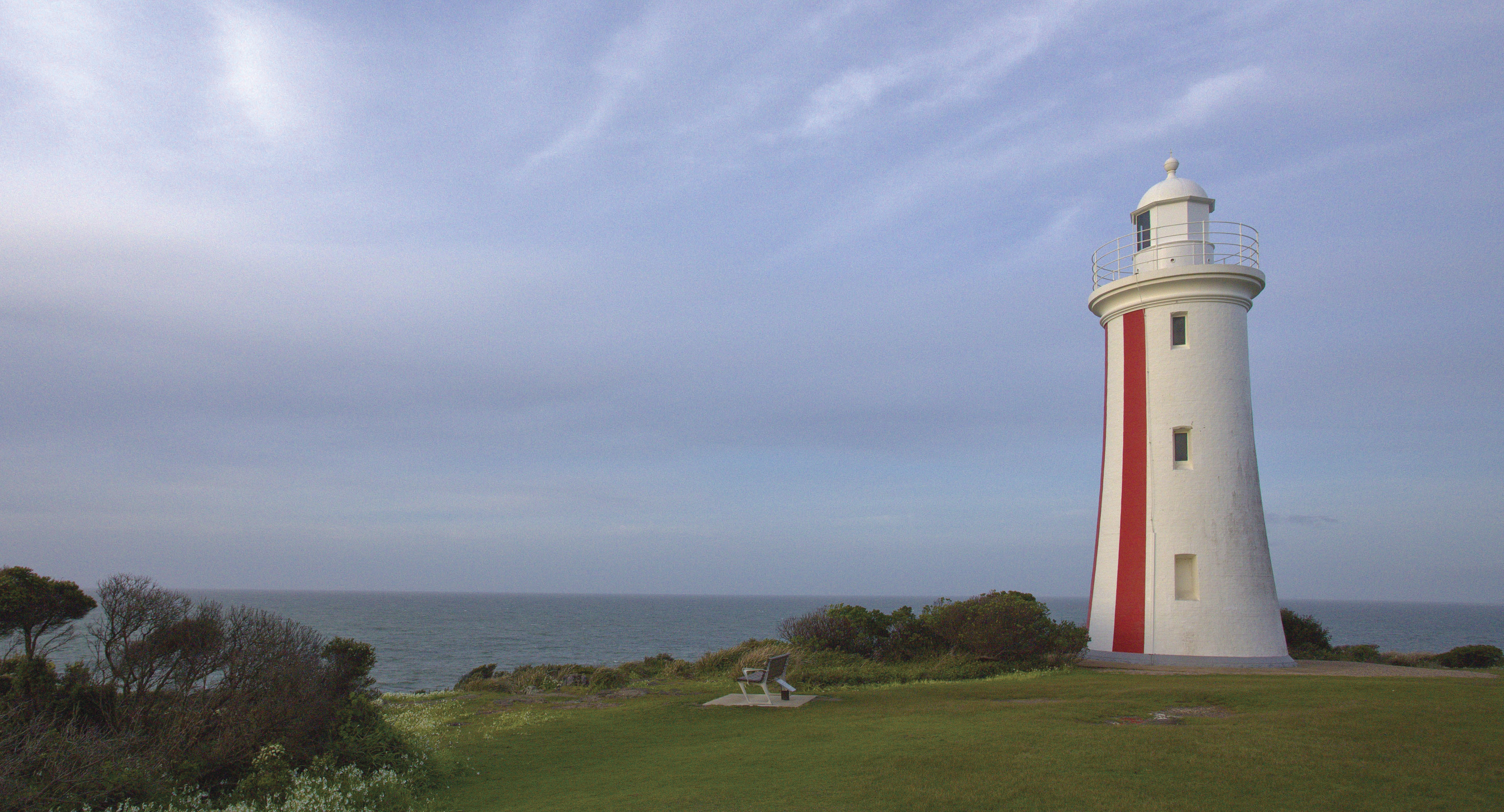 Image of Mersey Bluff Lighthouse that sits on a lush, green hill by the coastline.