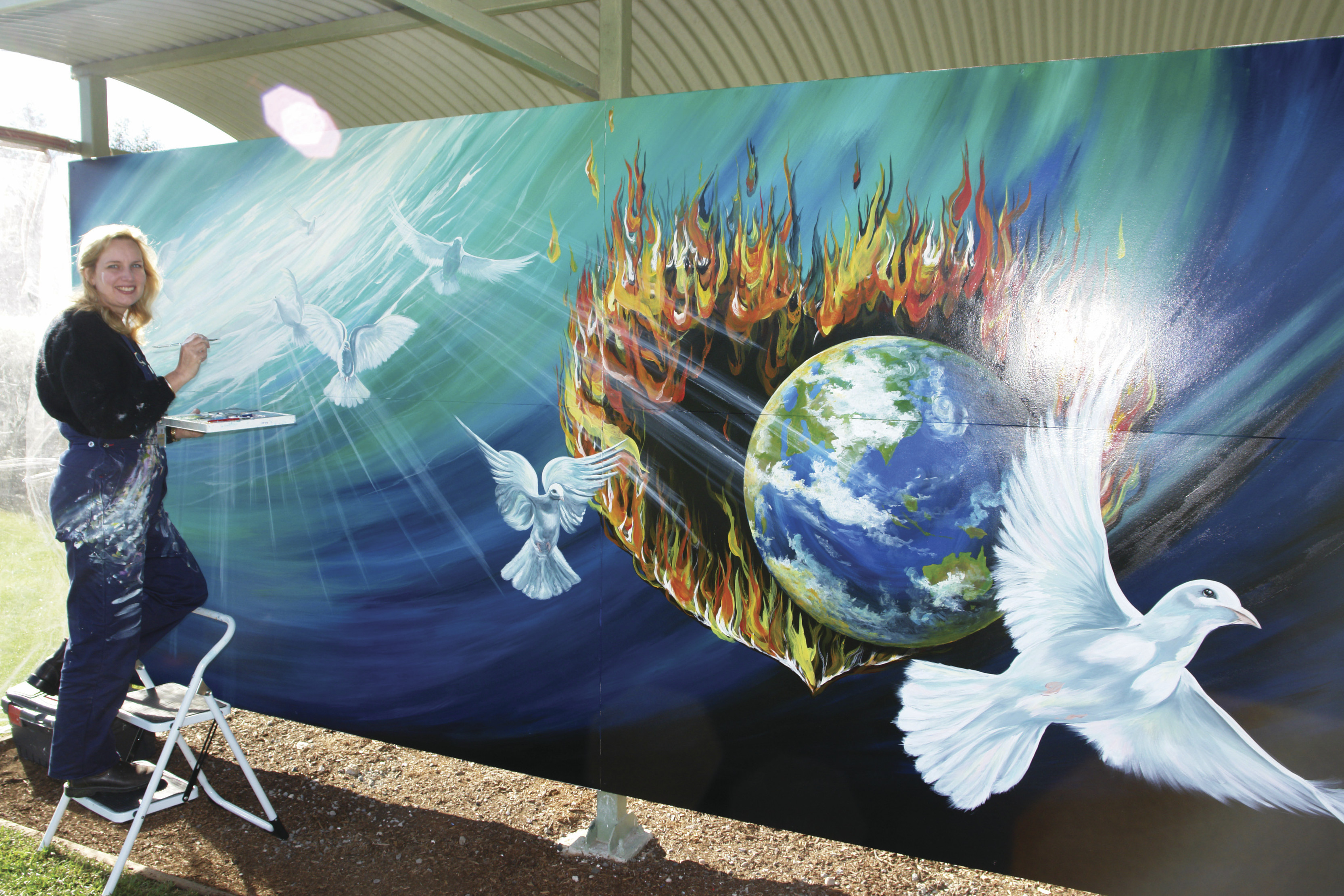 Lady Painting an amazing mural of the planet surrounded by fire, the ocean and birds, as part of the International Mural Fest.