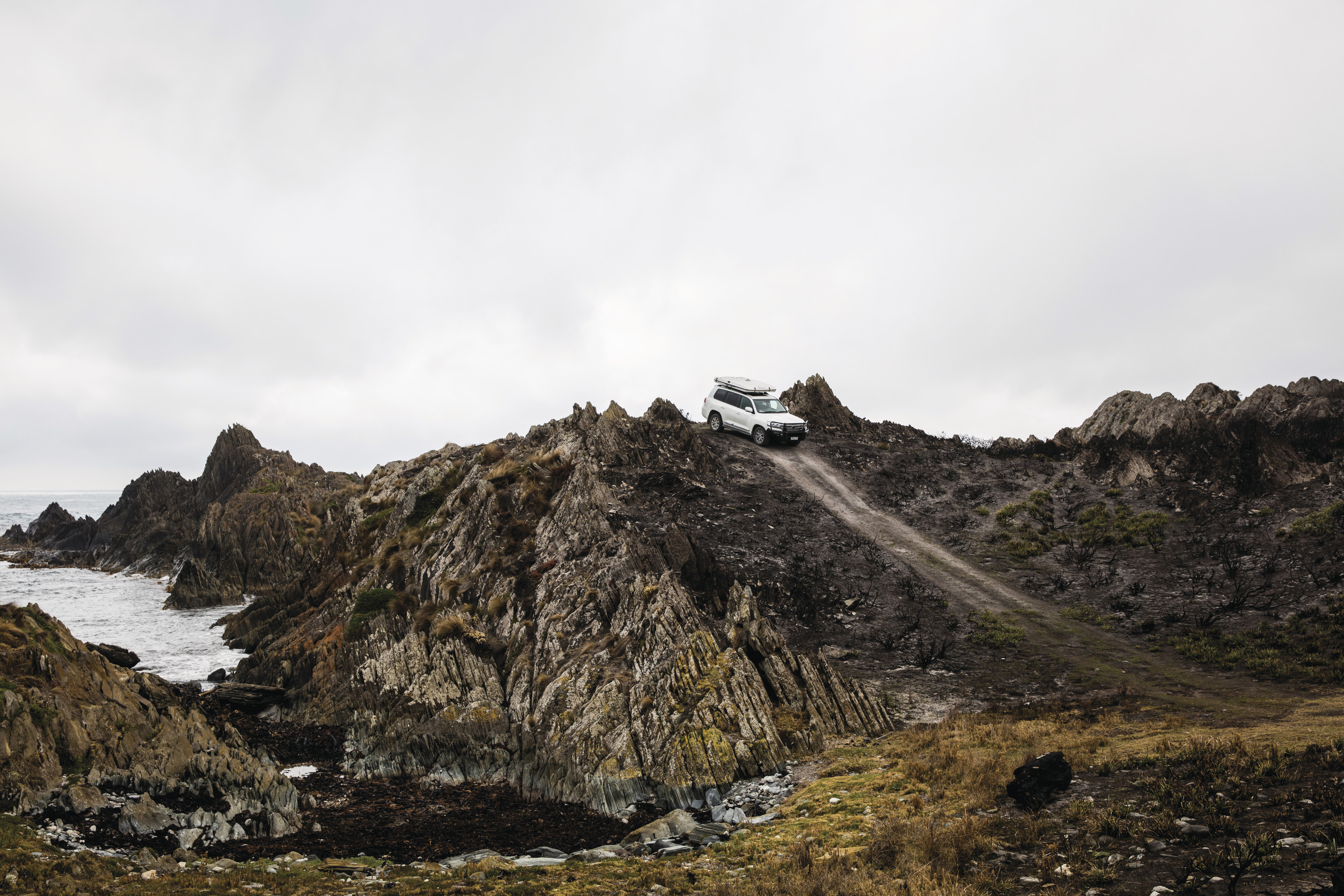 Car driving down a rocky road on Gardiner Point surrounded by rocks and grass on a cloudy day.