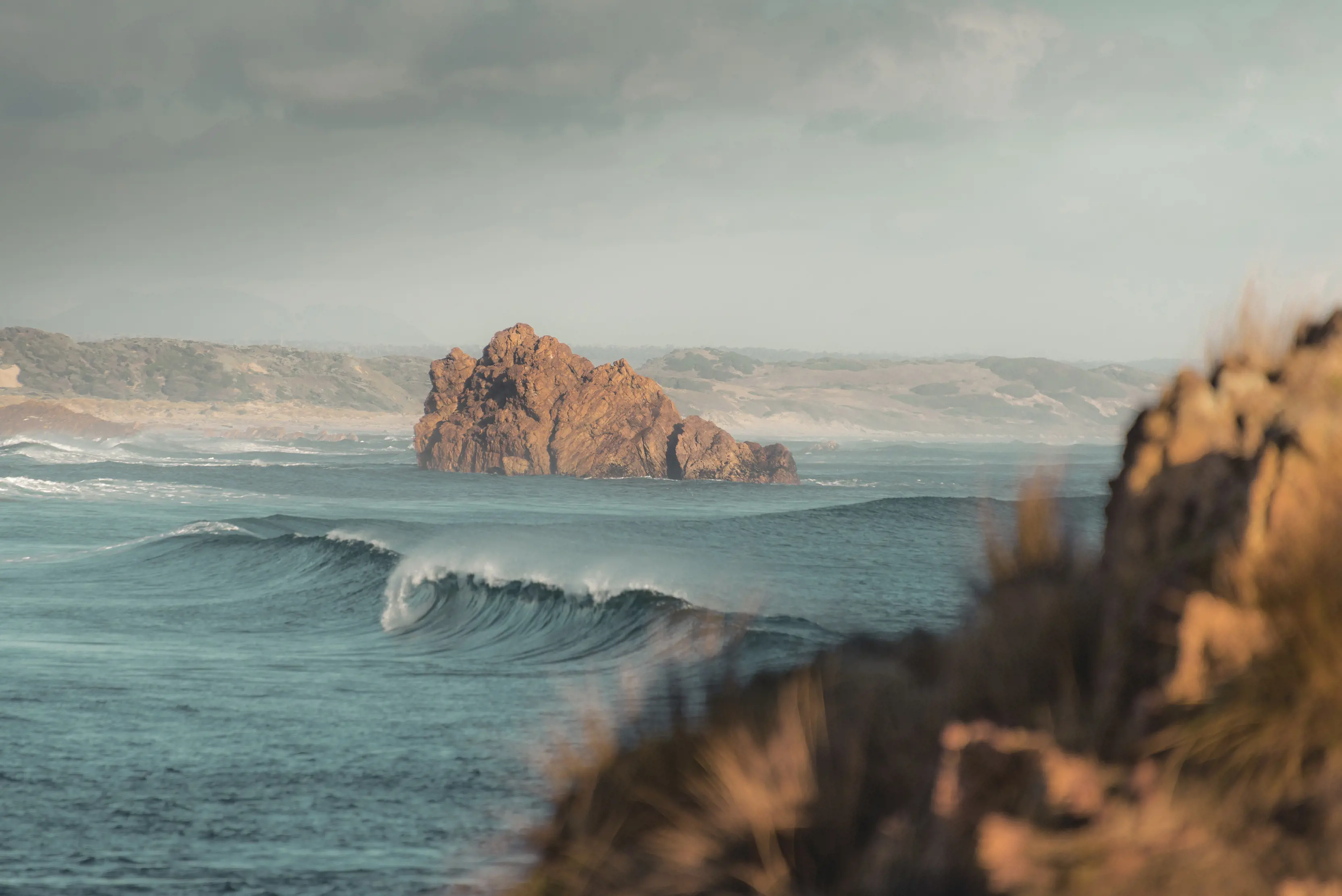 A vibrant image of a breaking wave with surrounding coastline in the background. Taken within the Arthur-Pieman Conservation Area.