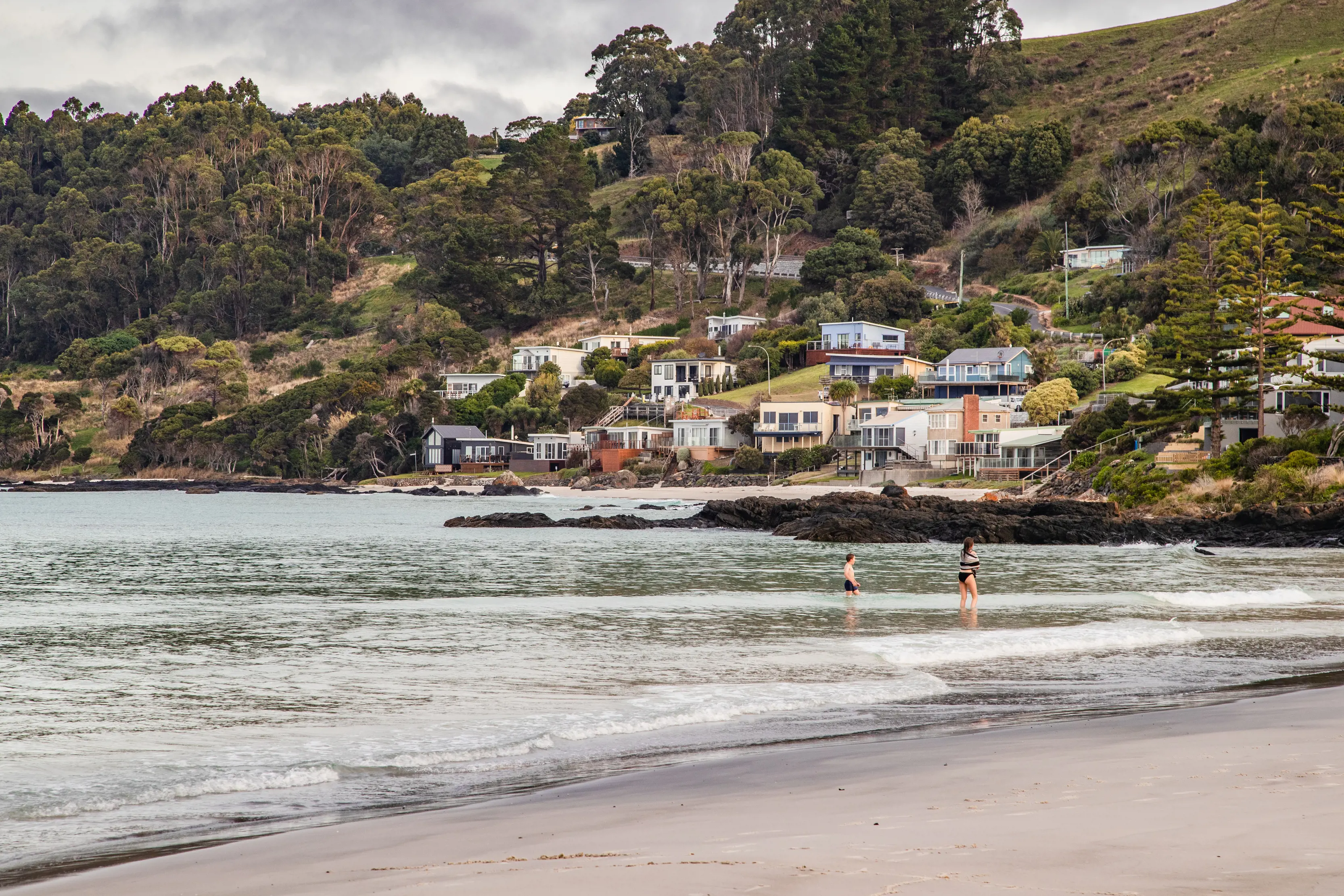 Two people in the ocean of Boat Harbour with houses and bushland surround the background.