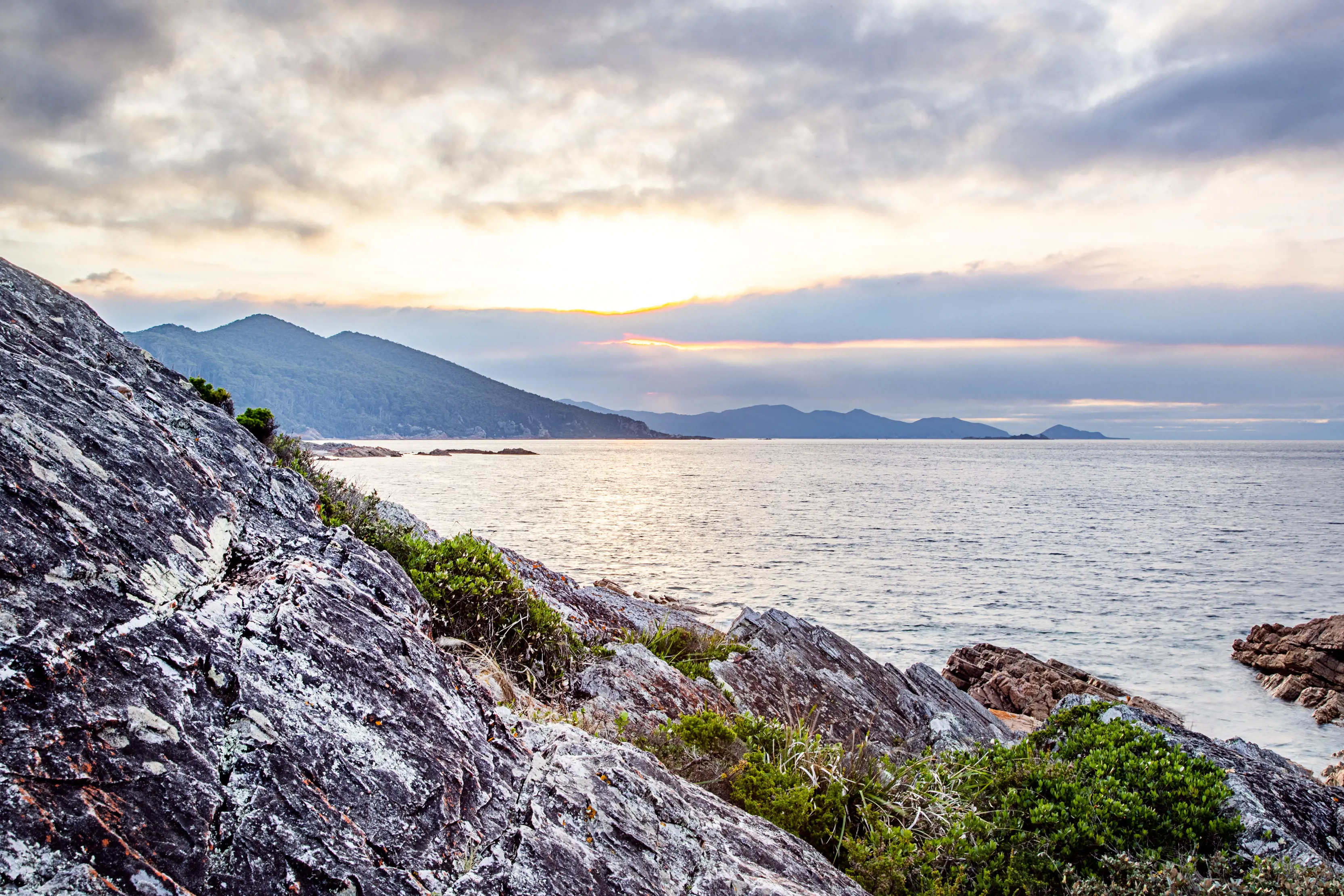 Rocky coastline fills the foreground of the image with the ocean and dramatic coastline in the background of Boat Harbour. 