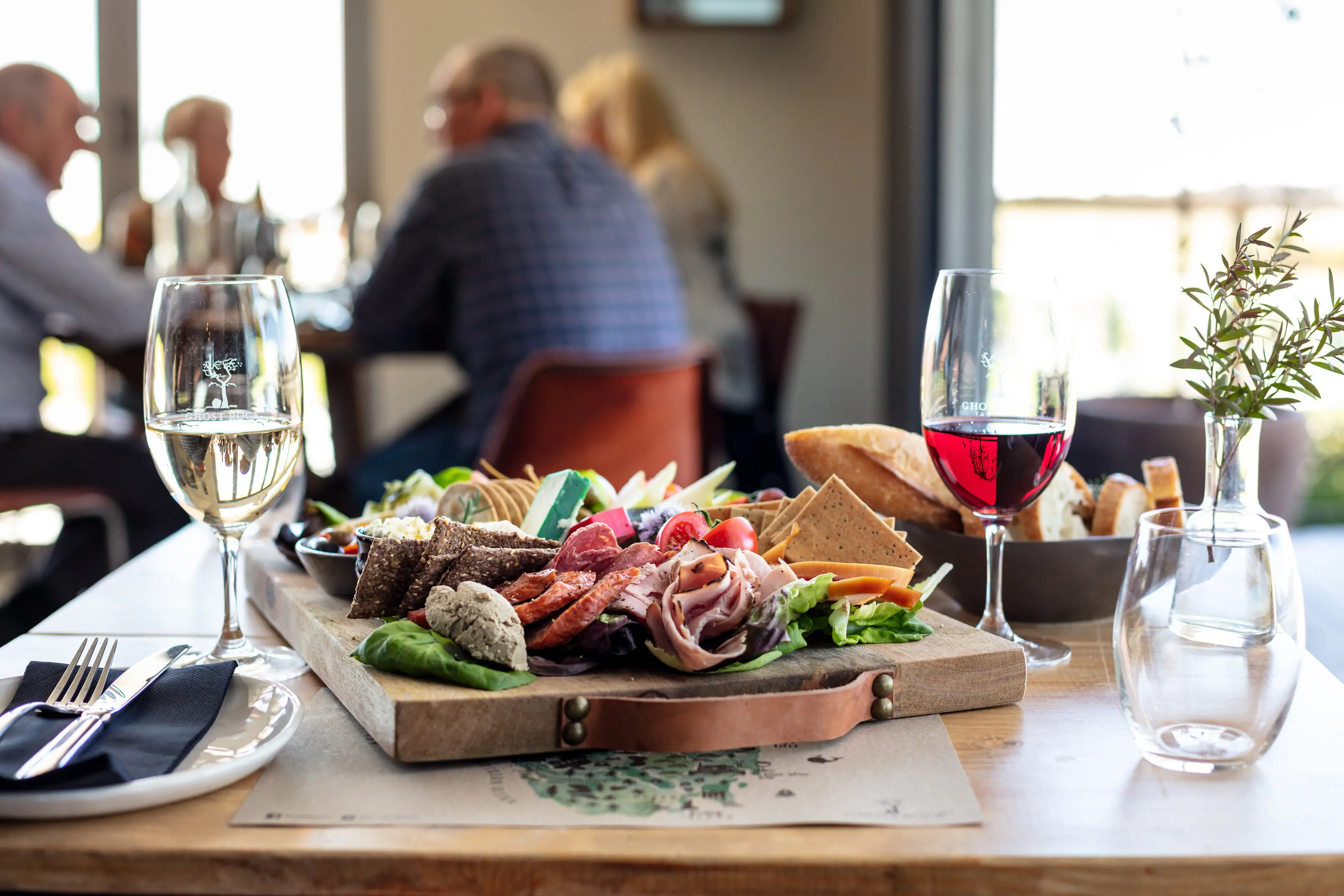 Image of a platter of a variety of fresh food accompanied with a bowl of bread and a glass each of red and white wine.