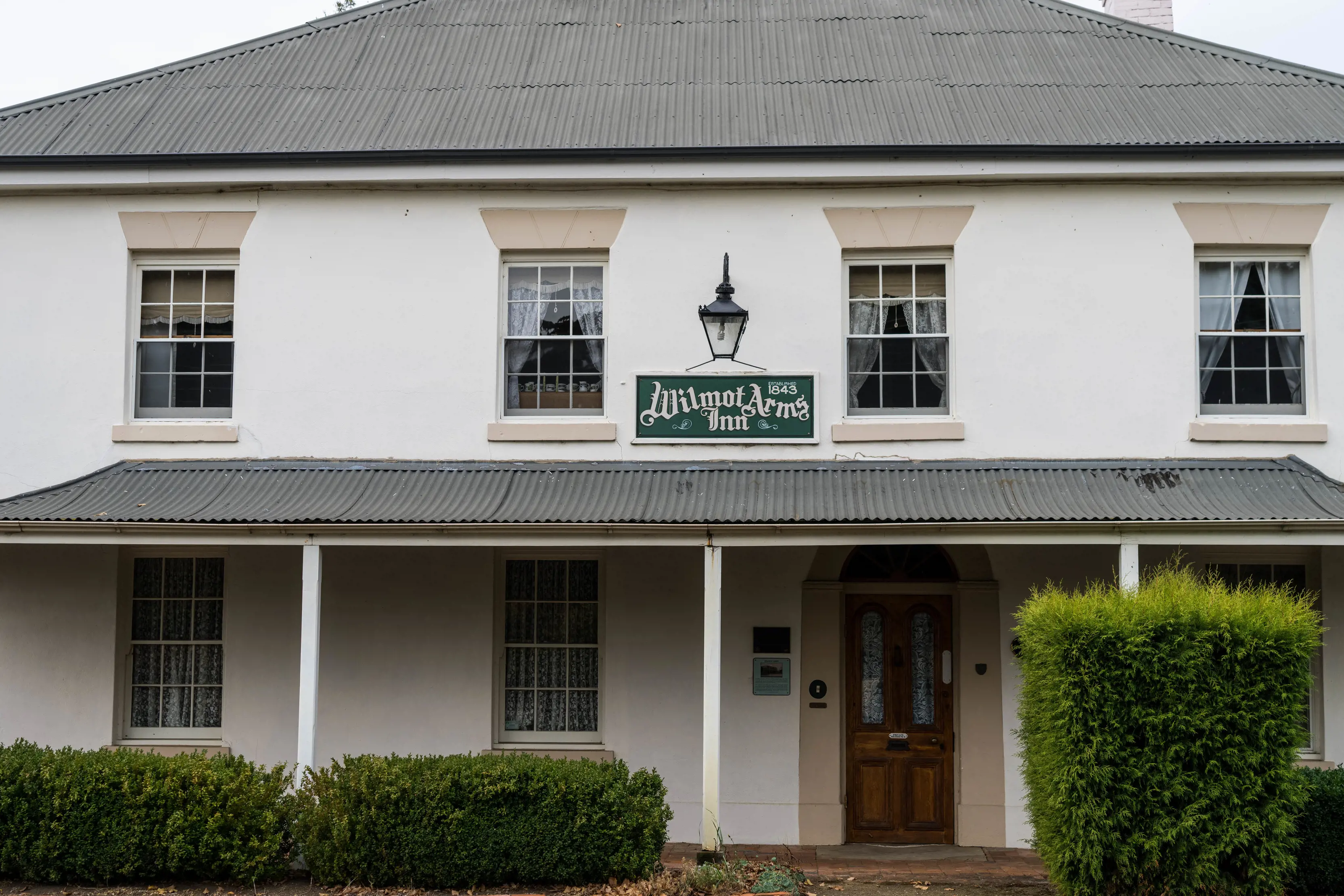 Image of the front of the Wilmot Arms Inn. A well looked after two story building with freshly trimmed hedges out the front. 