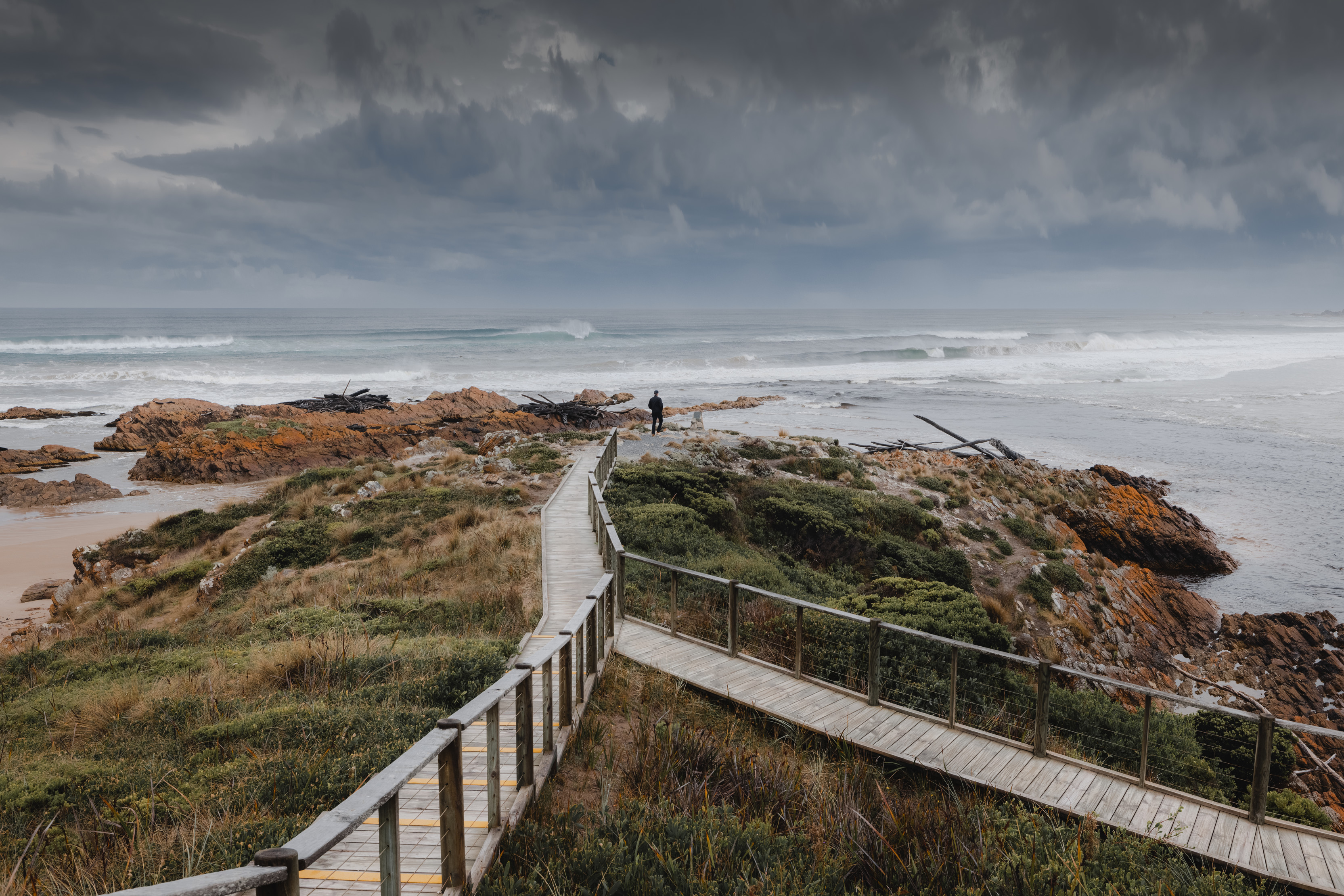 Image of Gardnier Point with wooden boardwalks surrounded by bush and rocks lead to the point with the ocean in the background.