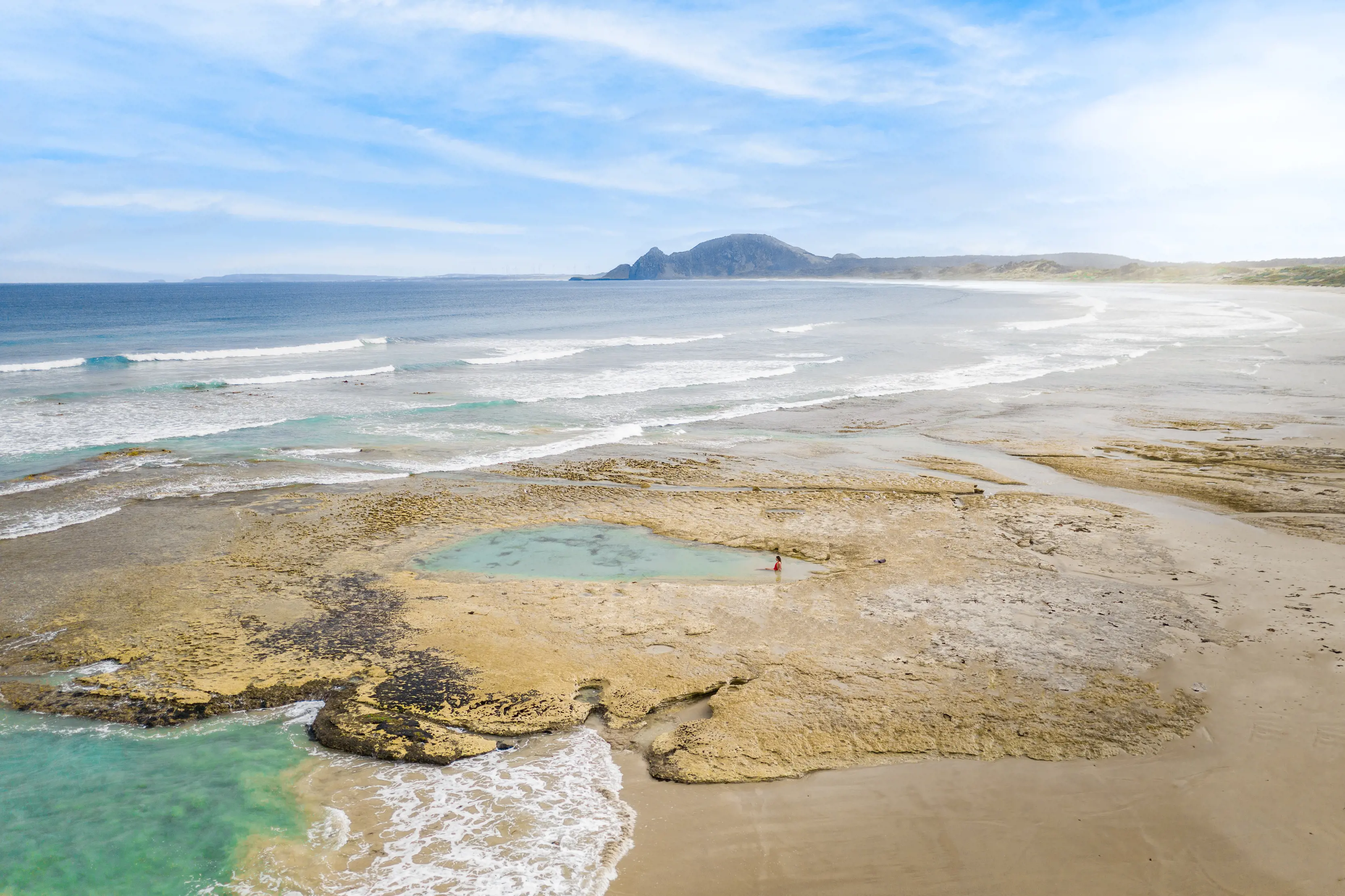 Incredible aerial image of a person enjoying a dip in a rockpool by Green Point Beach, Marrawah, on a clear, summer's day.