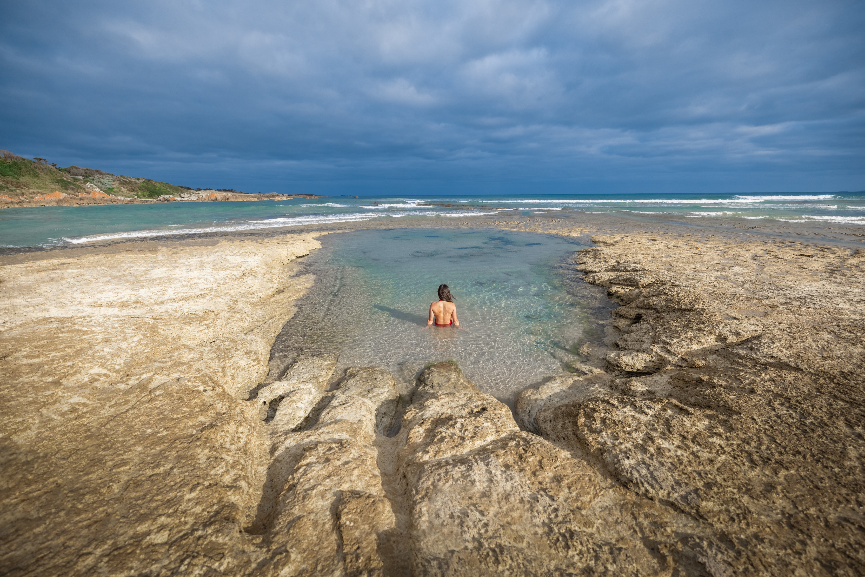 Incredible wide angle image of a person enjoying a dip in a rockpool by Green Point Beach, Marrawah, on a clear, summer's day.