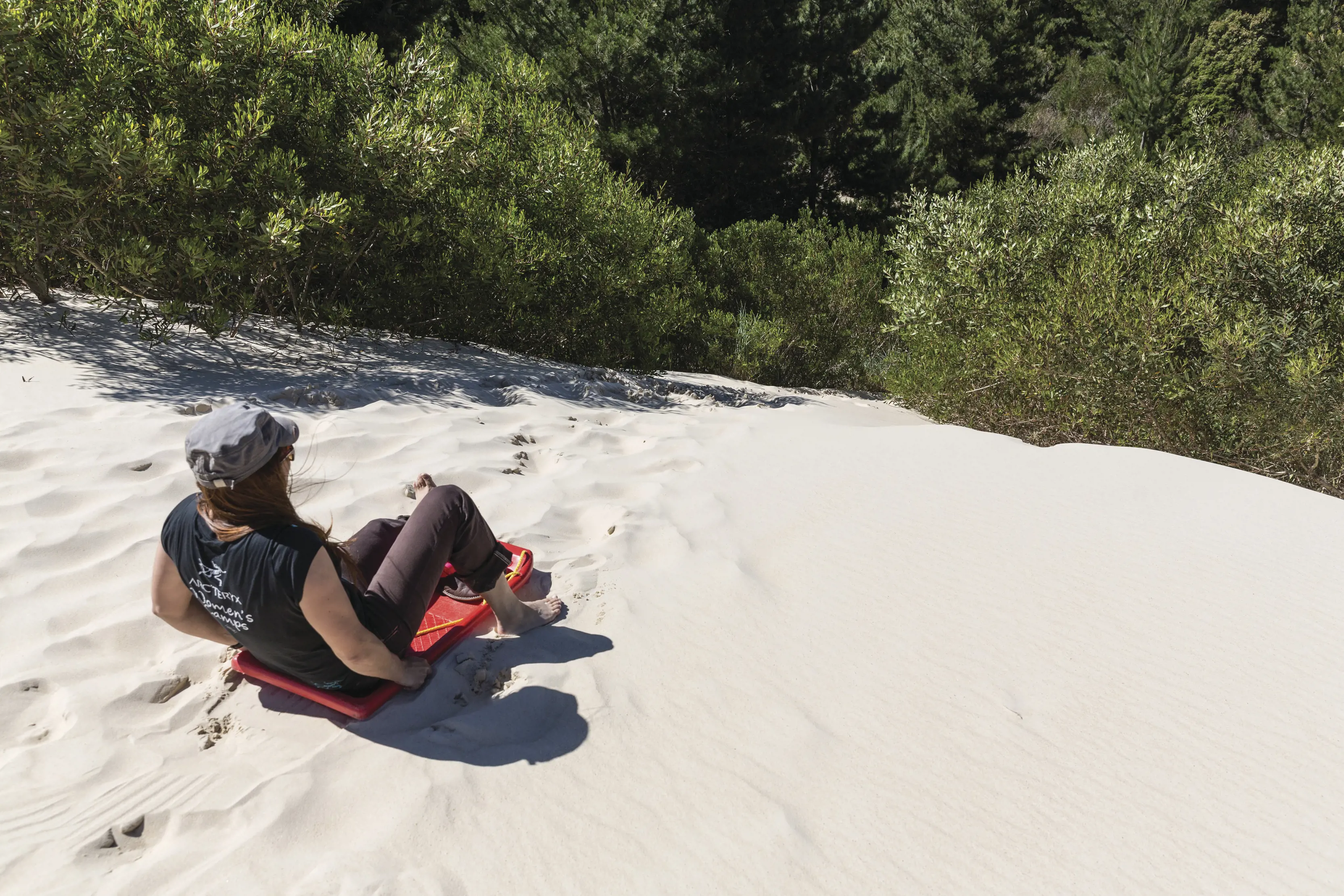 A woman enjoys tobogganing at Henty Dunes, riding down the sand dunes on a red board.