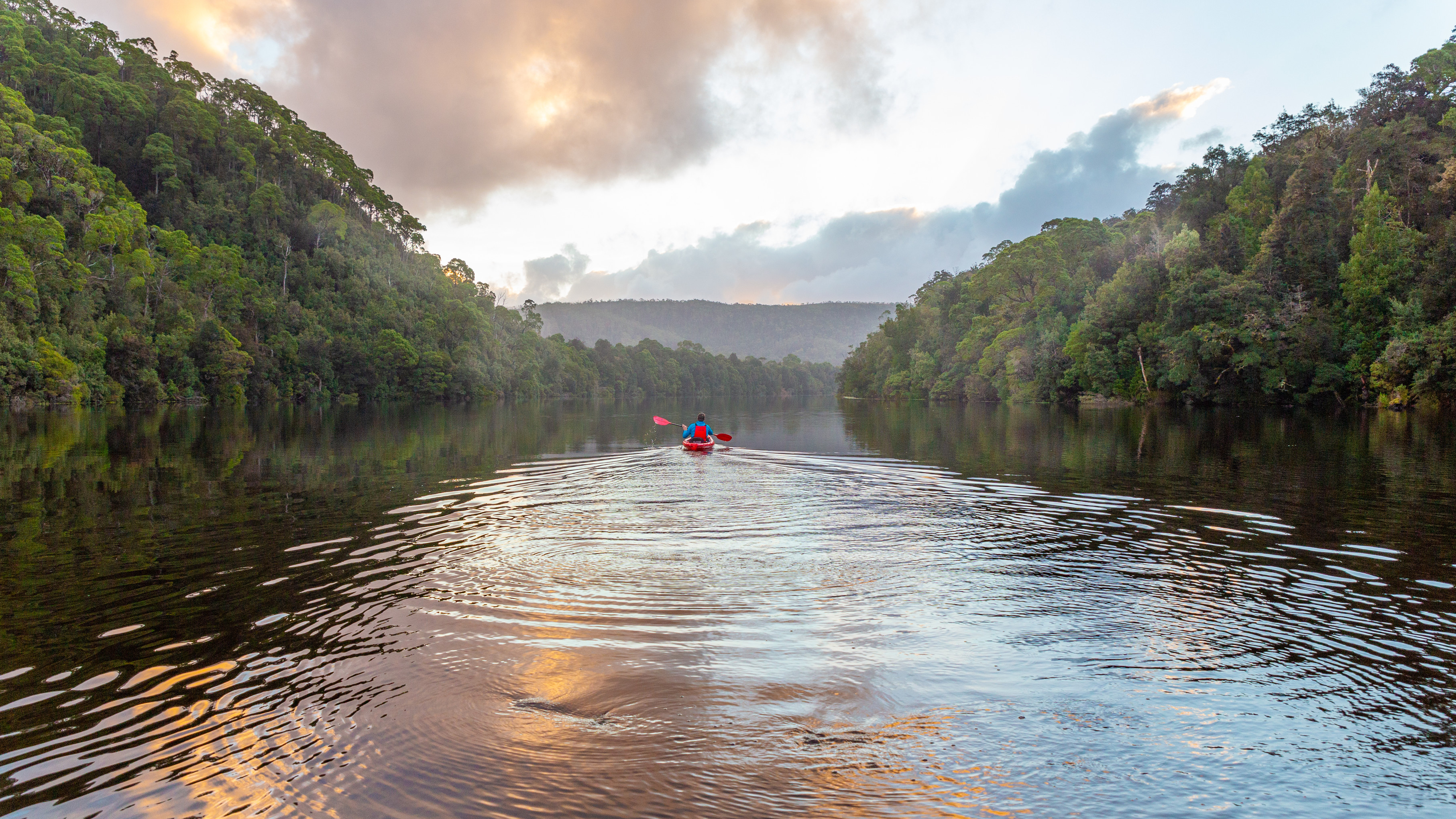 People Kayaking on the Pieman River. The river is mirror-like and reflects the cloud-filled sky.