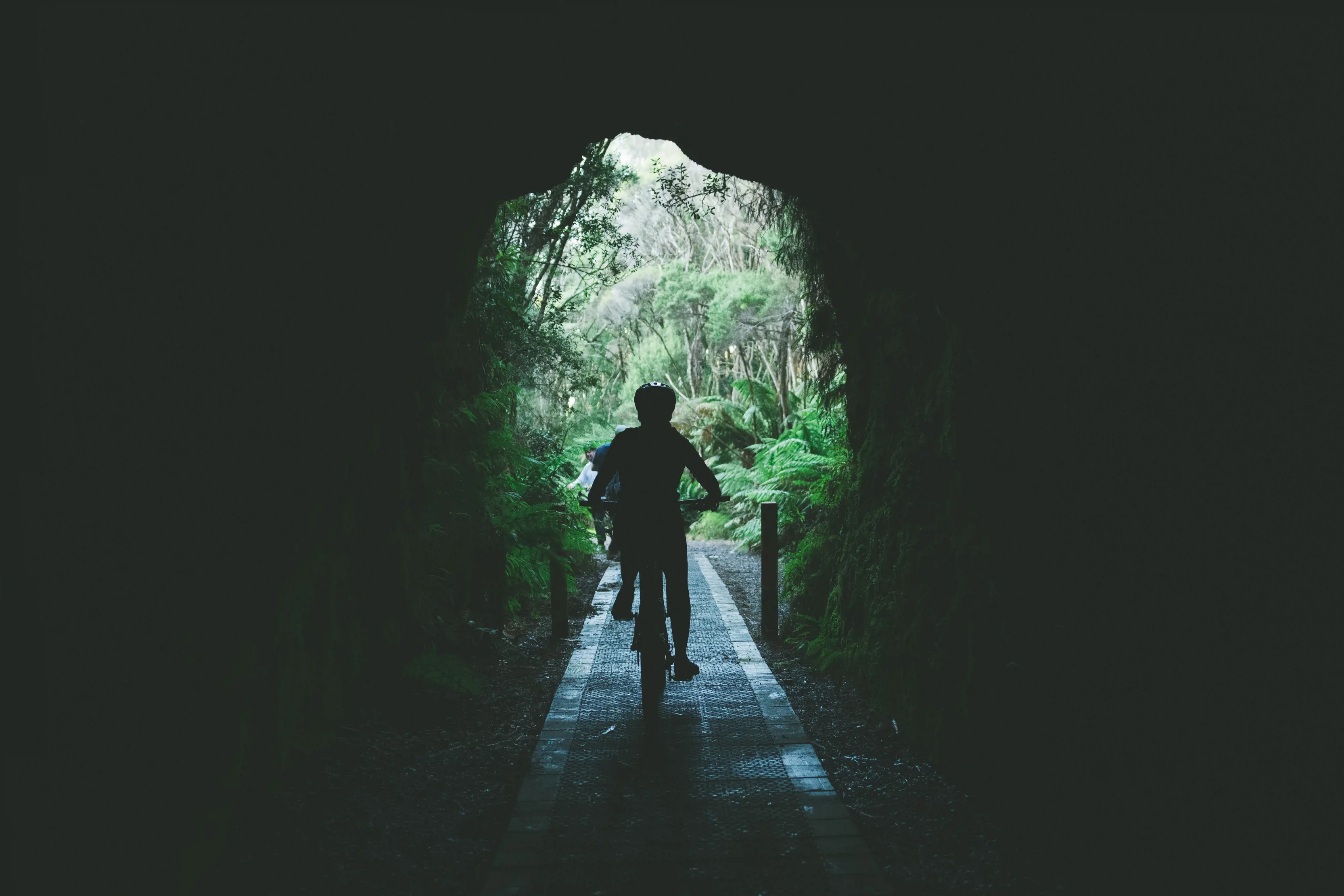 Mountain biker rides through the Spray Tunnel, taken from inside the dark tunnel with the opening at the end of the tunnel visible.