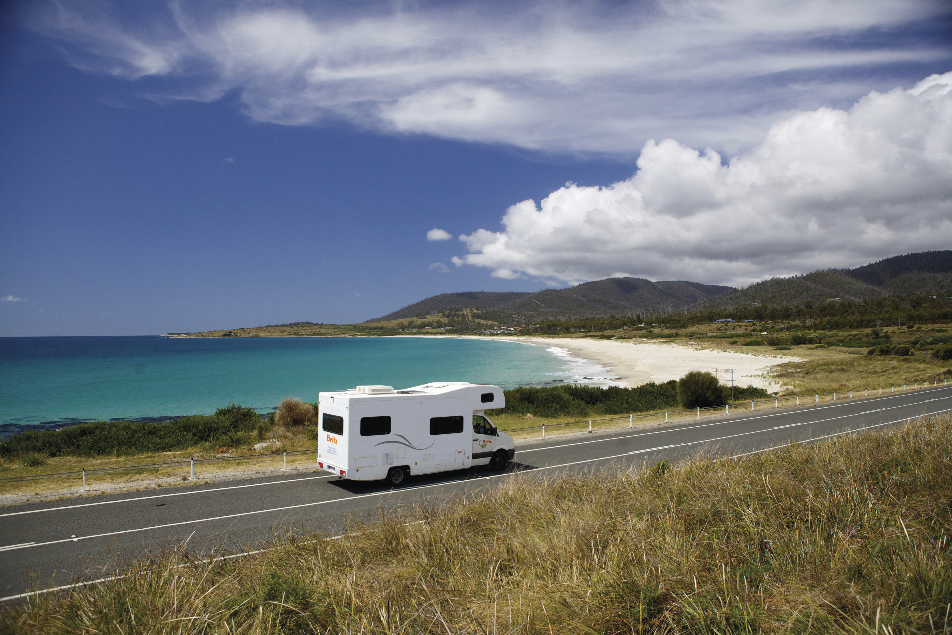 A white campervan drives along the waterfront road whilst touring Four Mile Creek.