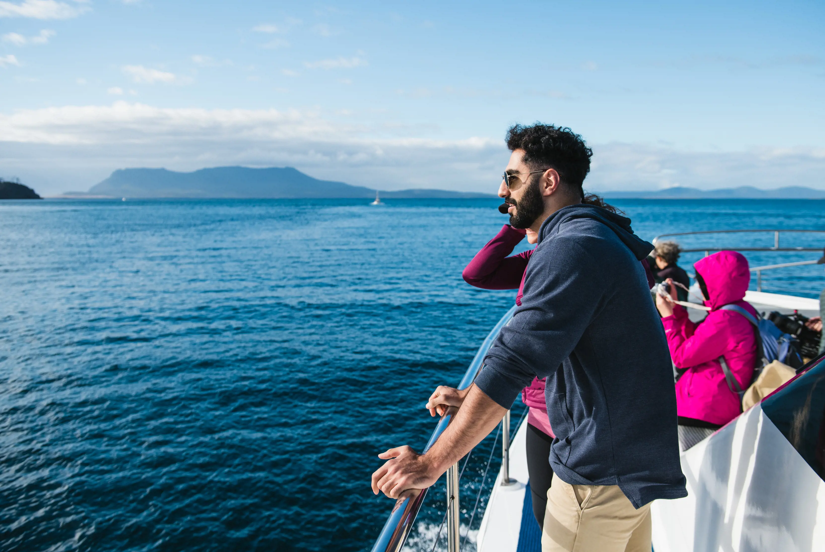 A group of people aboard the "Encounter Maria Island" ferry, sail across pristine, blue ocean, admiring the beautiful scenery.
