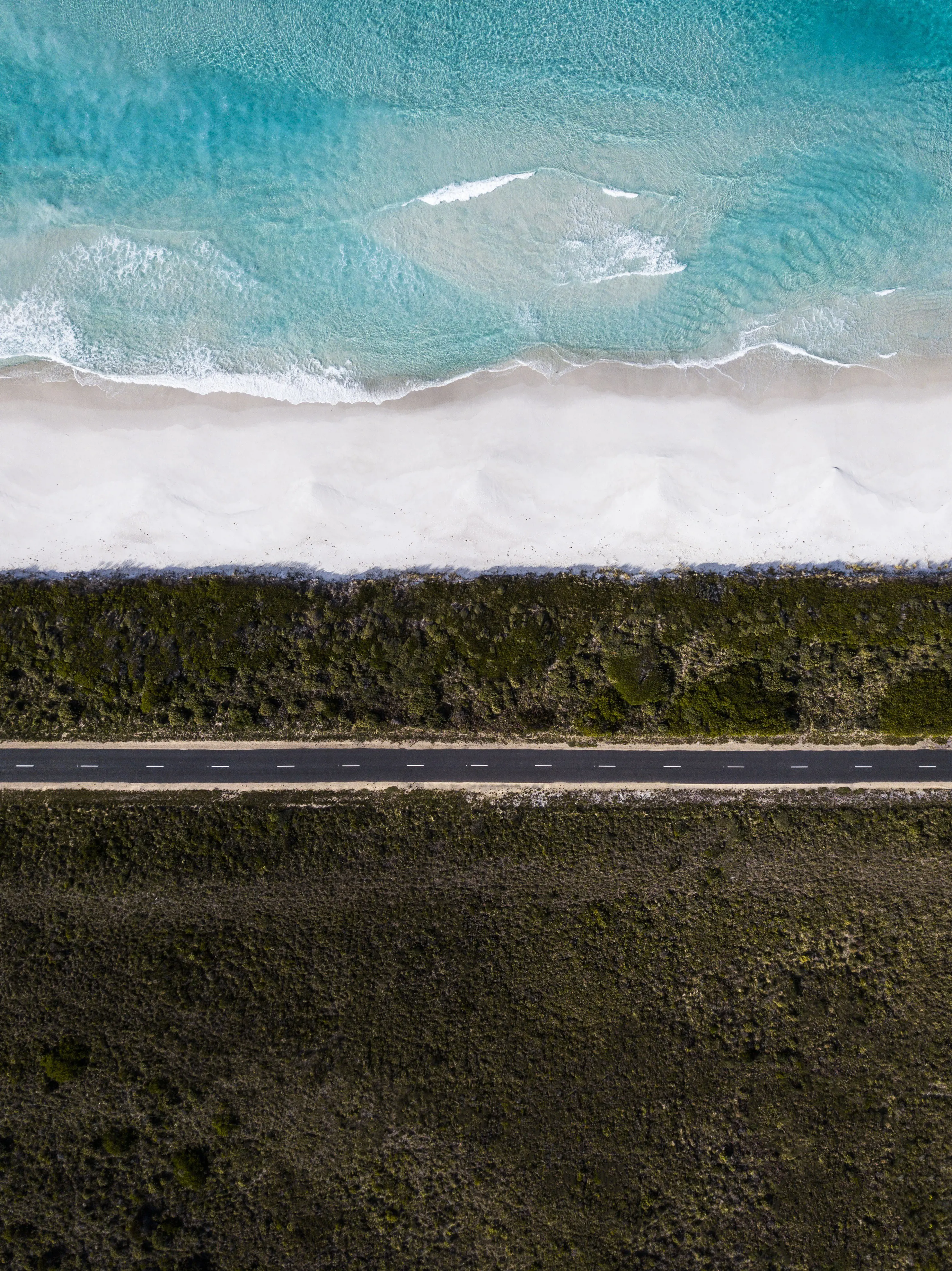 An incredible aerial view of the Road to Bicheno, with the stunning shoreline and ocean on one side and lush bushland on the opposite.