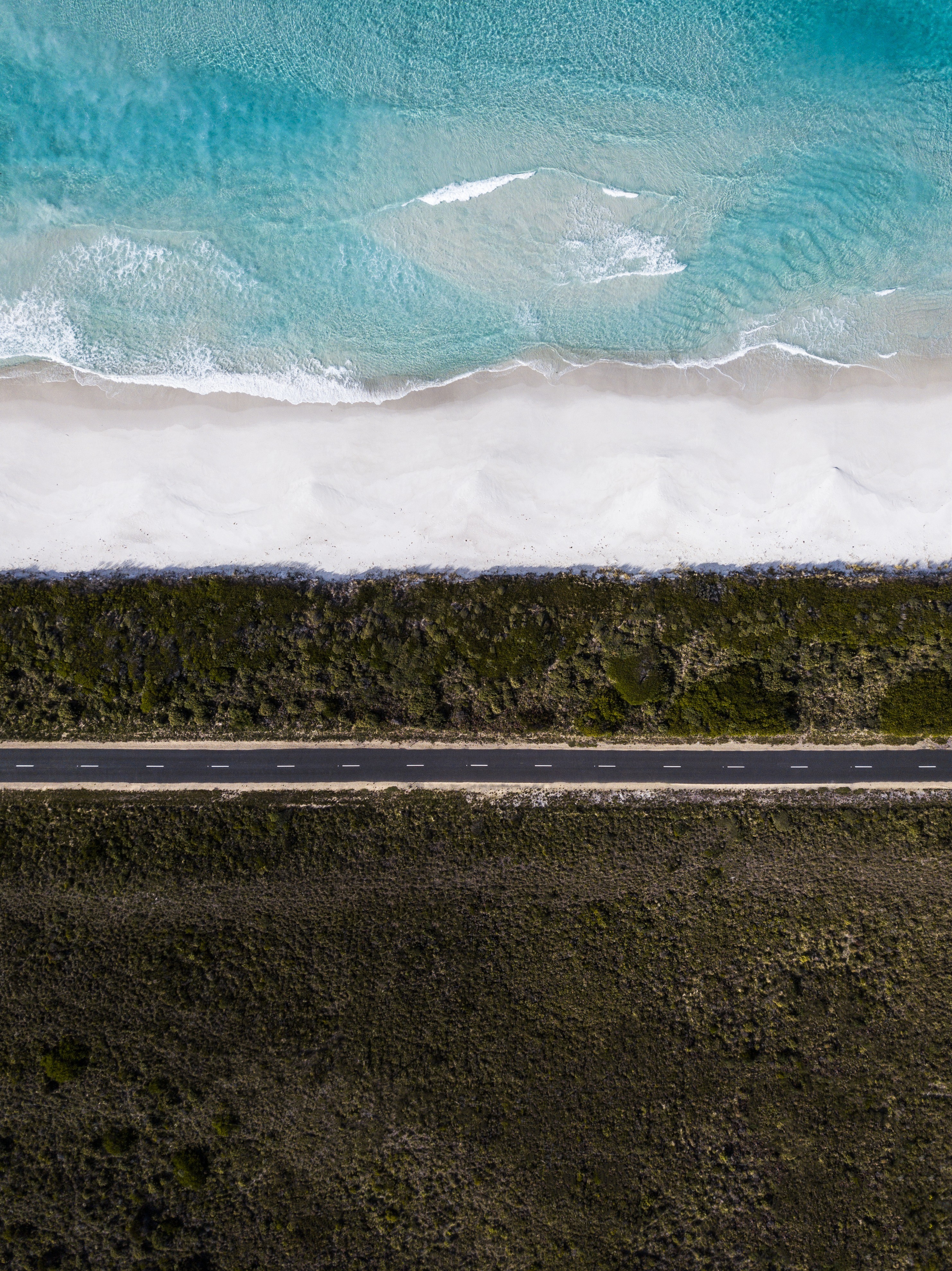 An incredible aerial view of the Road to Bicheno, with the stunning shoreline and ocean on one side and lush bushland on the opposite.
