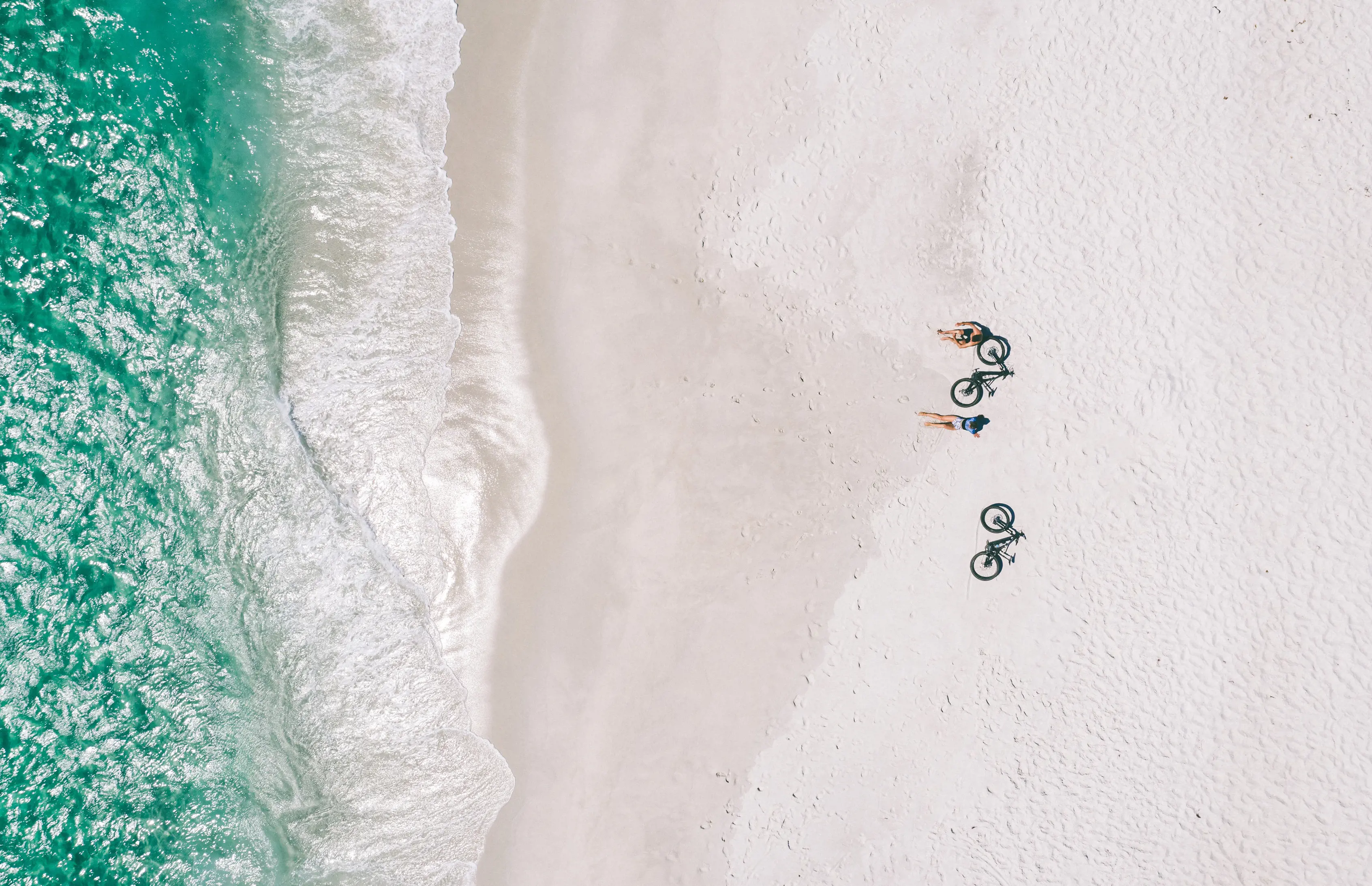 Ariel looking down over a beach at St Helens, two cyclists rest on sand with their bikes placed next to them facing the water.