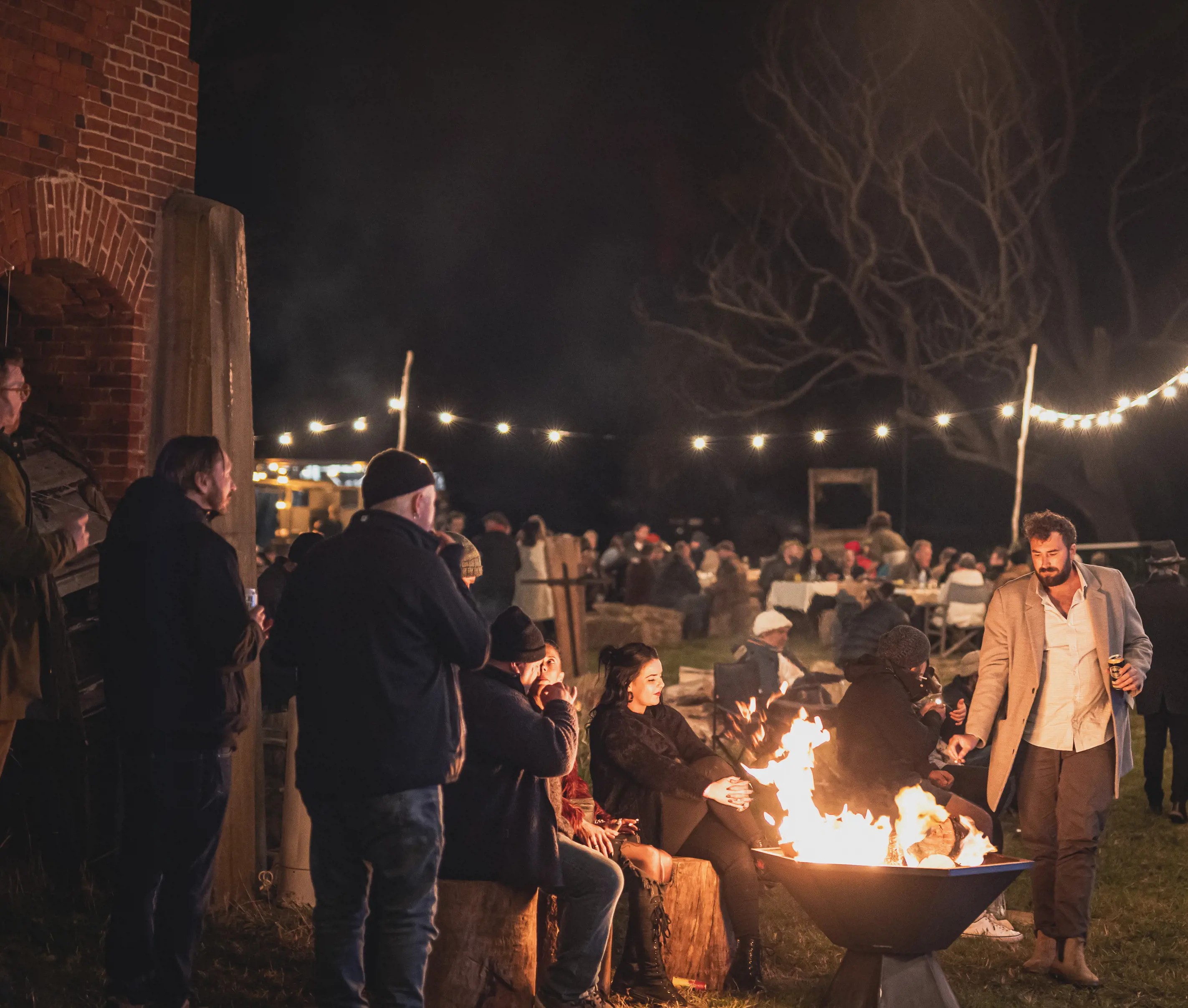 Crowds sit by a burning fire outdoors at East Coast Harvest Odyssey.