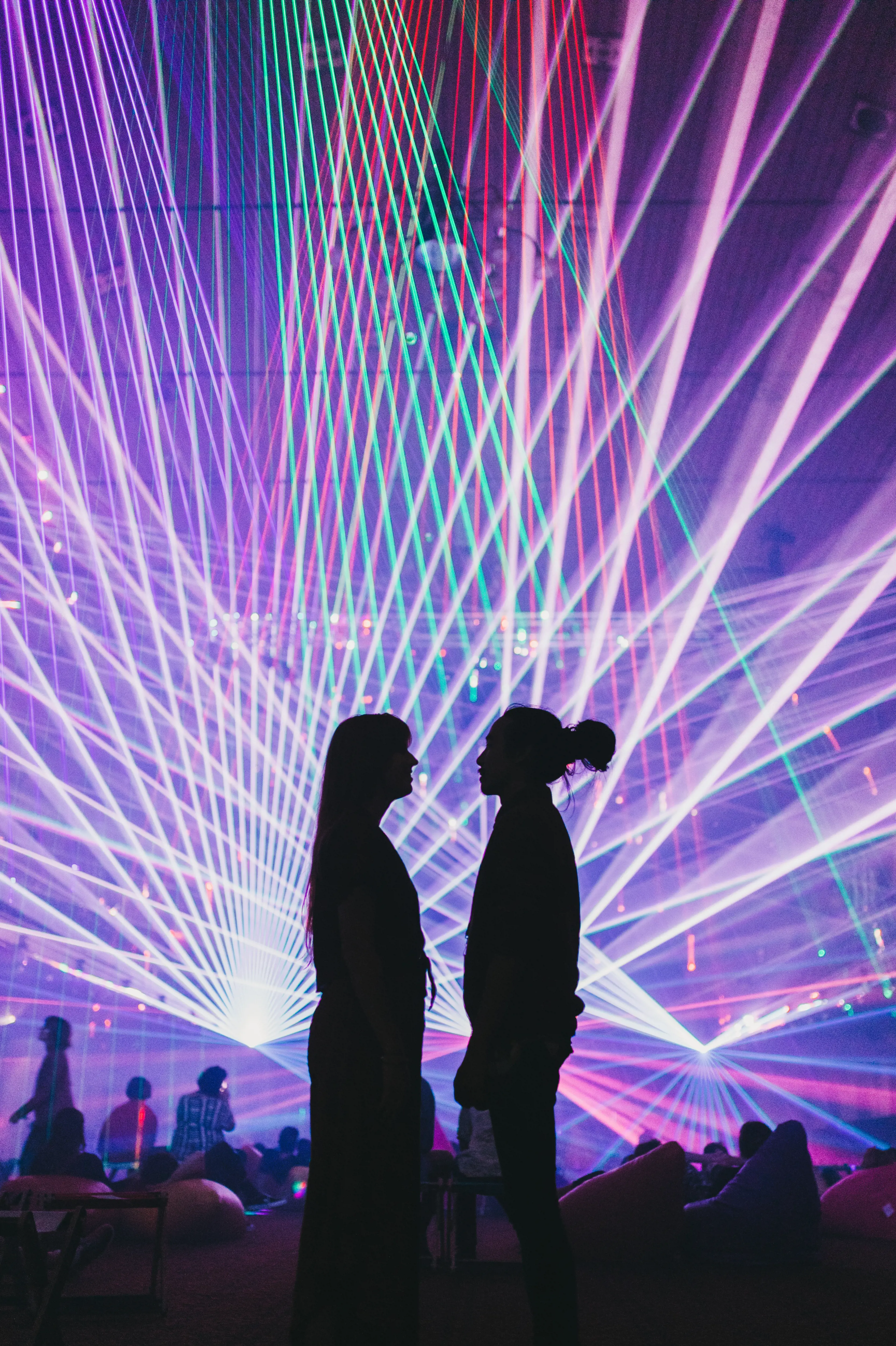A couple stand in a dark room lit by multi-coloured lasers.