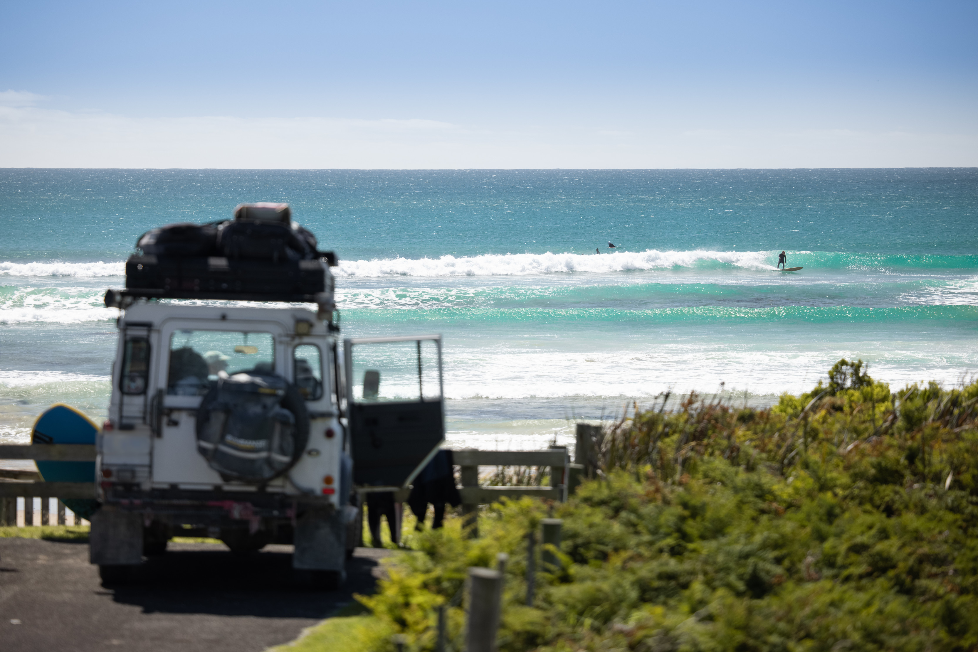 A white car parked up at taypalaka / Green Point Beach, Marrawah. Surfers are in the background.