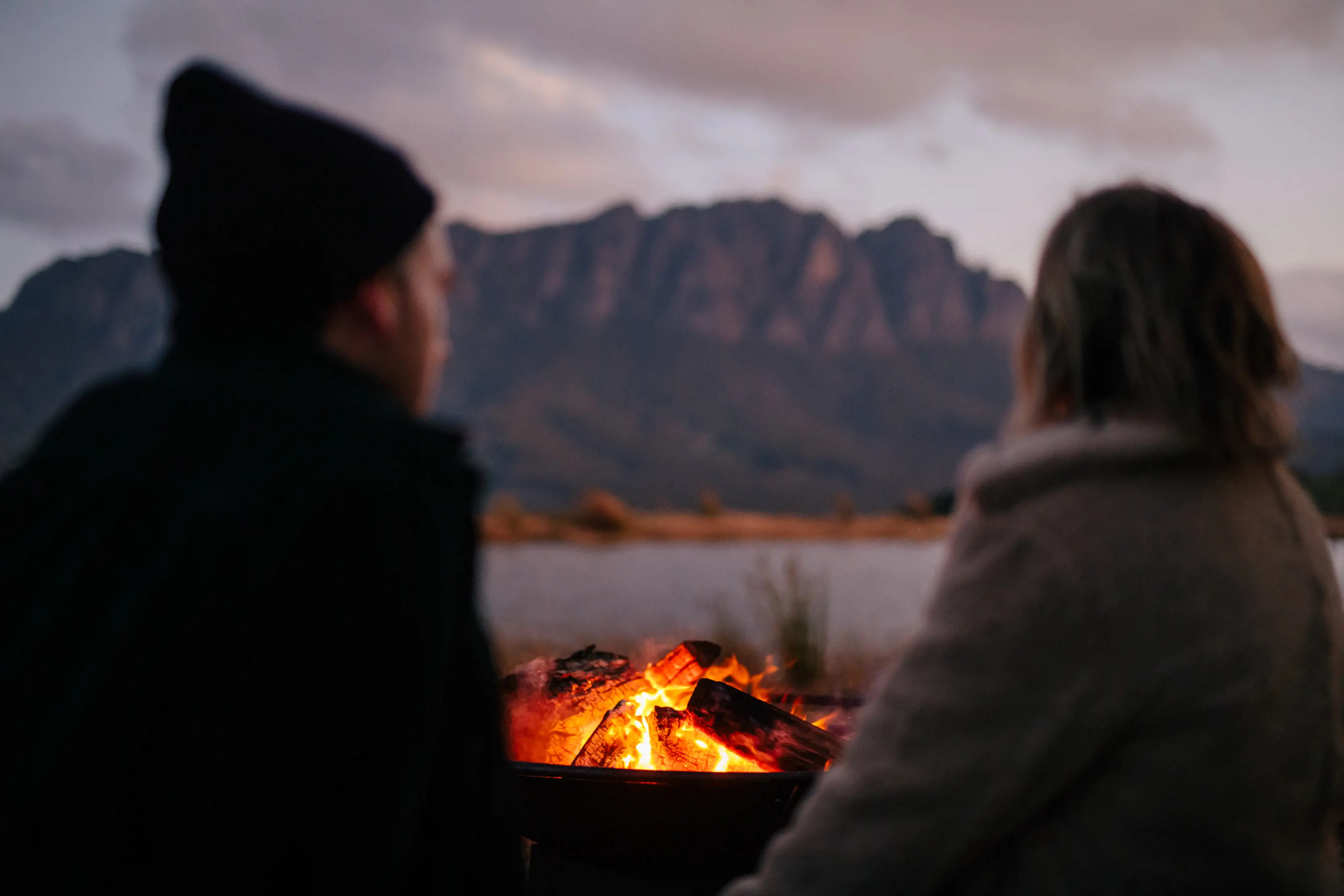 Two people sitting infront of a camp fire, looking out unto the mountains at the Eagles Nest Retreat