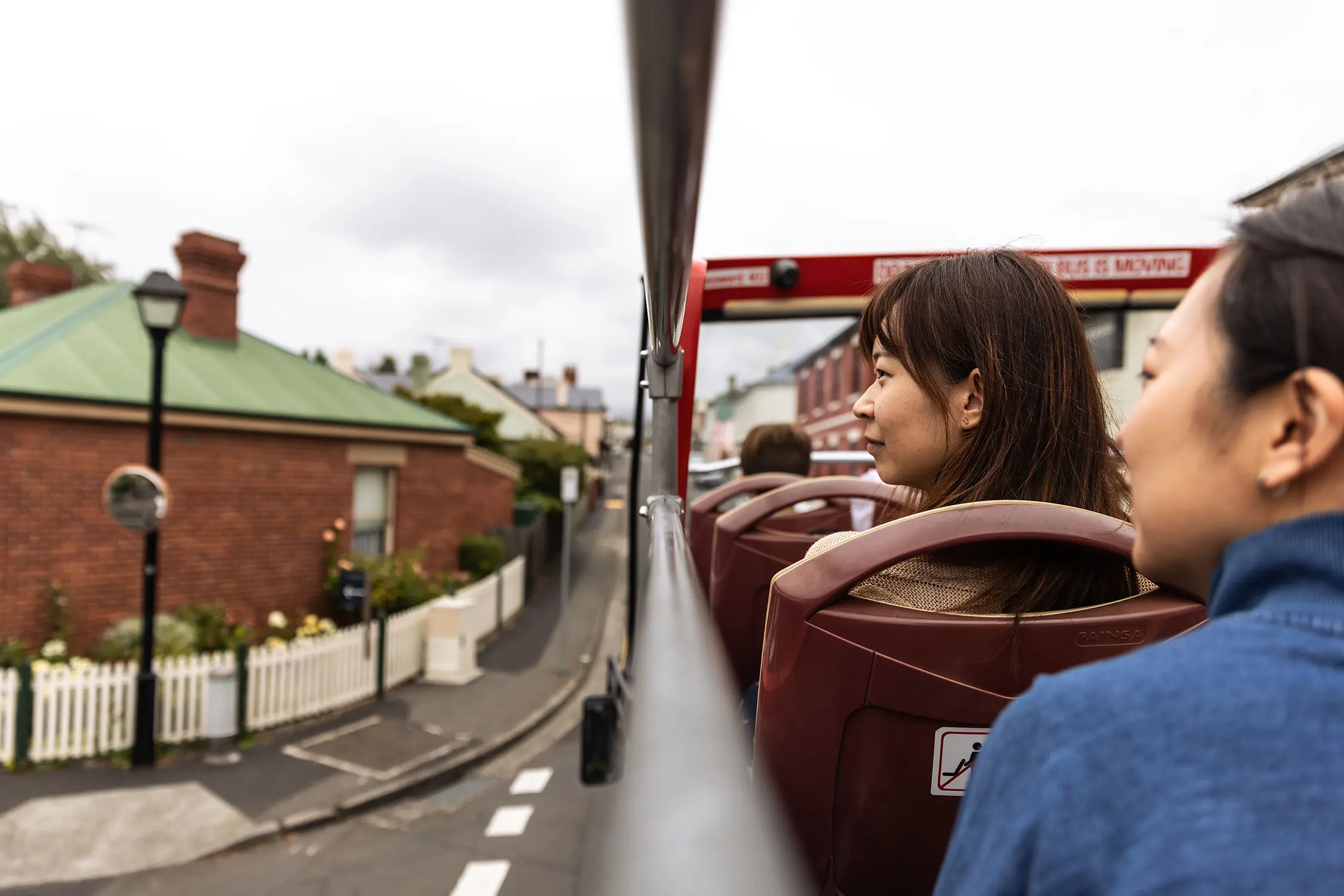 Looking over the side of a double-decker tourist bus, people sit in the seats on the open-air second level, looking out to a historic street.