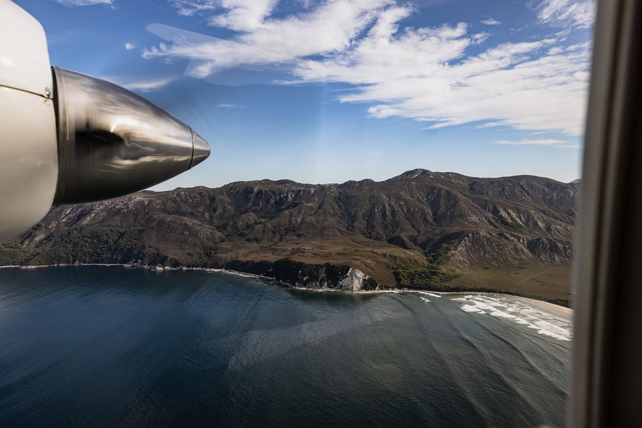 Looking through the window of a small sightseeing plane, over remote mountainous wilderness rising above an inlet.