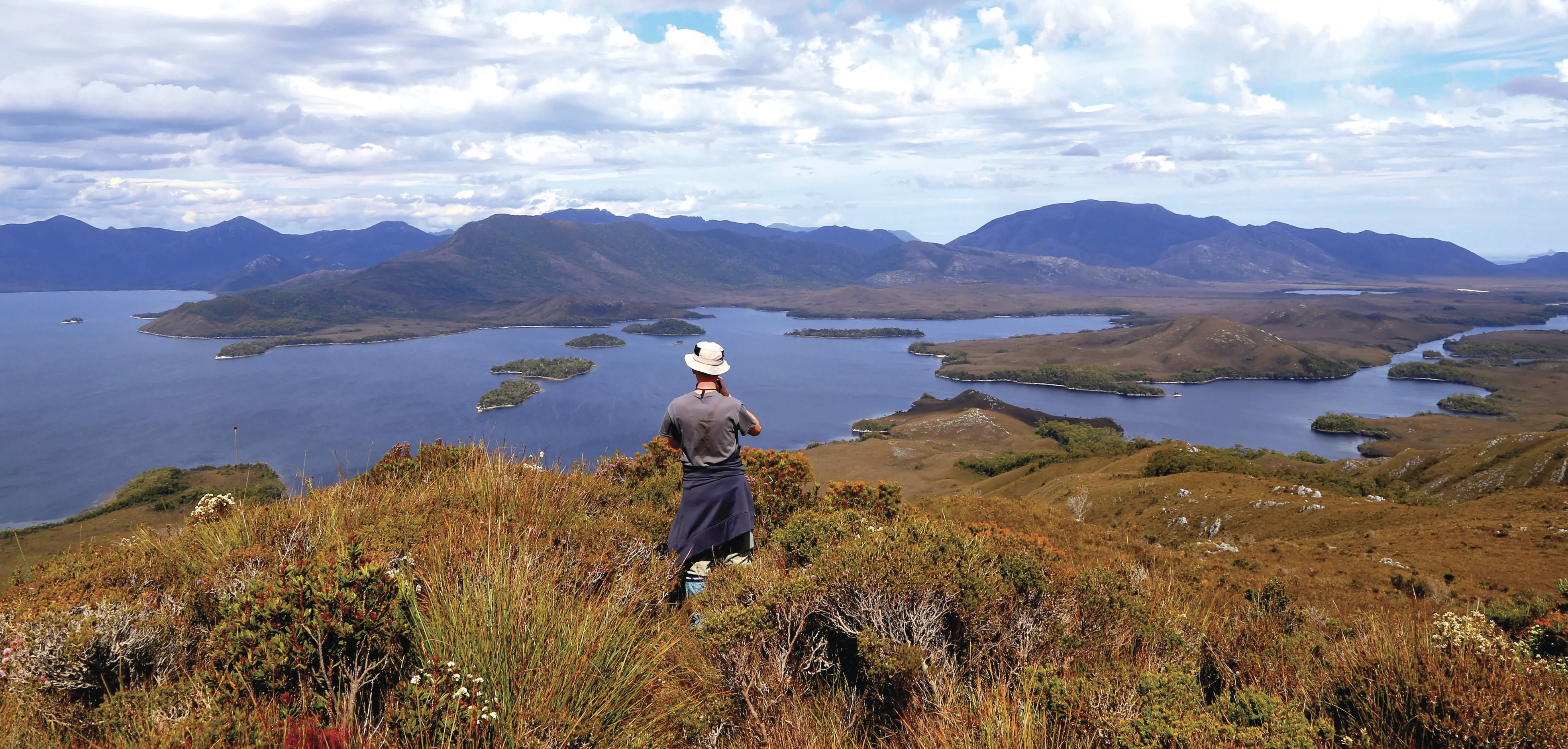 "Person at a peak of a mountain, exploring the incredibly remote waterways and wilderness of Bathurst Harbour/ Port Davey. "