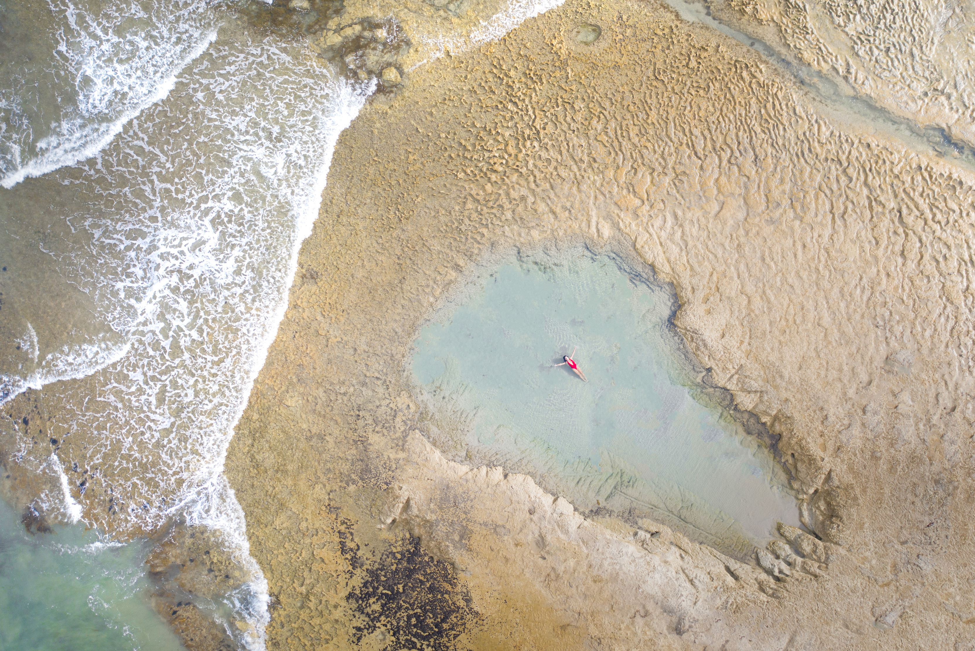 Incredible aerial image of Green Point Beach, showing a person swimming in a large rock pool, soaking up the sun.