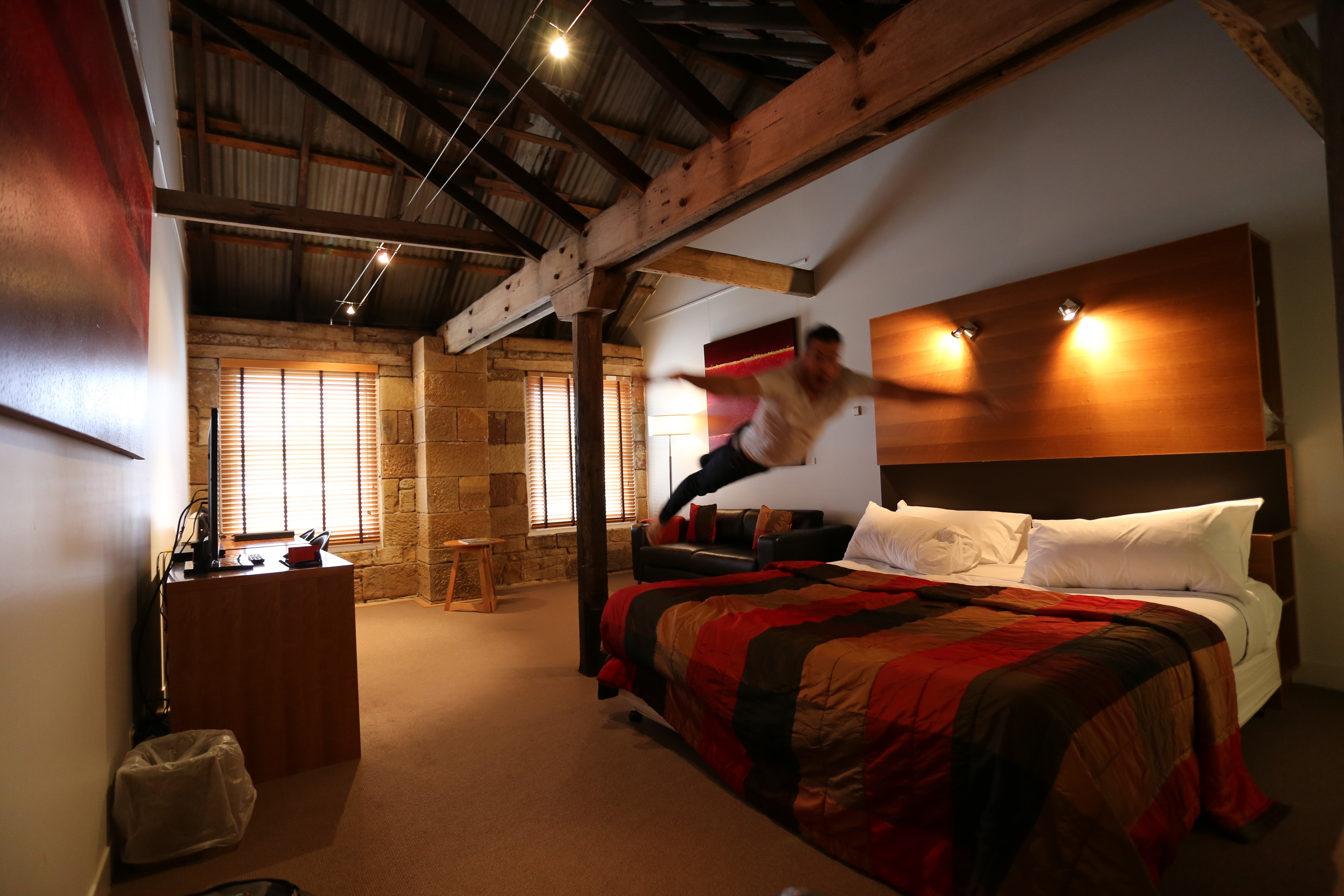 Image of bedroom suite at The Henry Jones Art Hotel. Room has high dark wooden beams on the ceiling and a warm glow