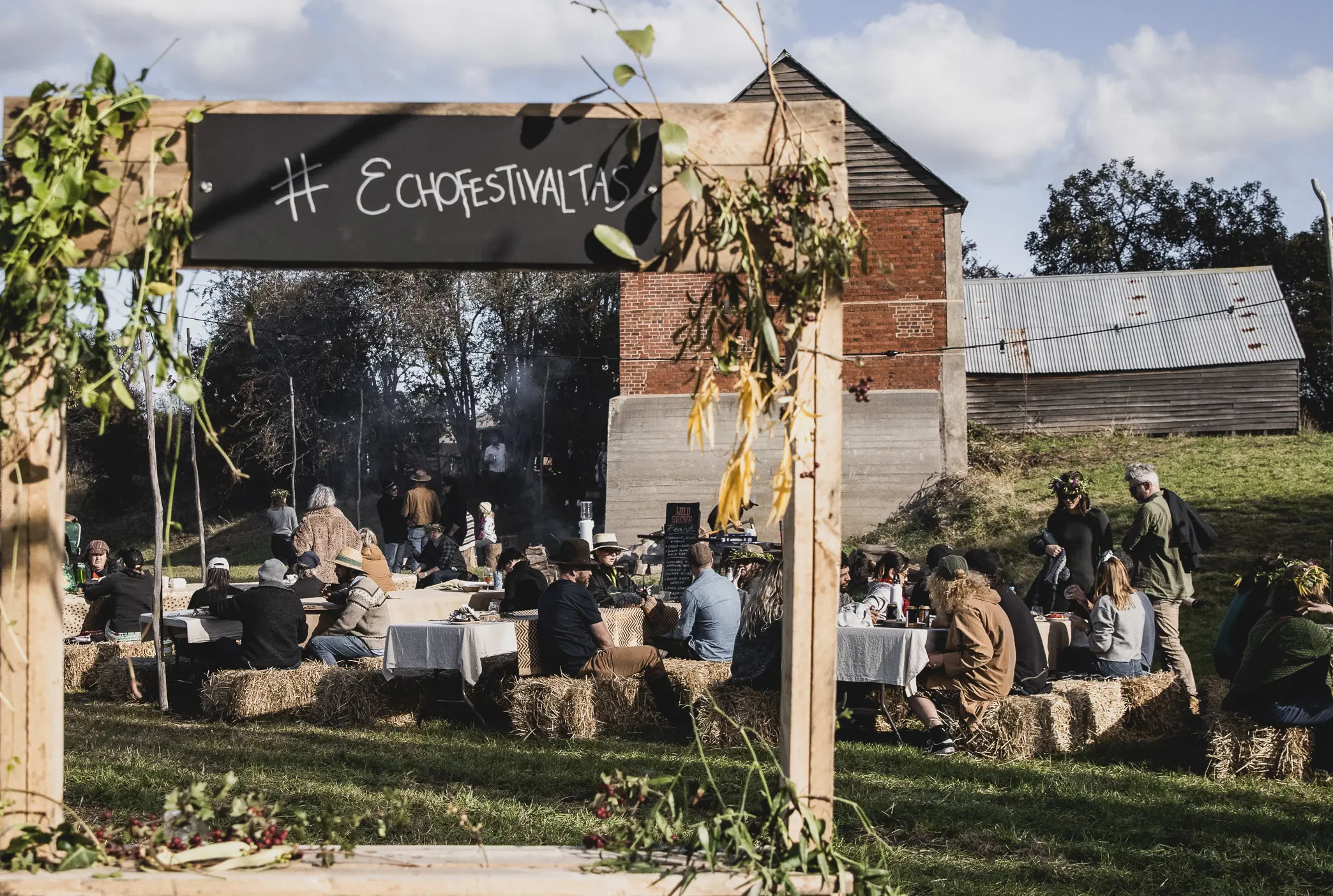 group of people sitting around tables and bales of hay enjoying entertainment near signage