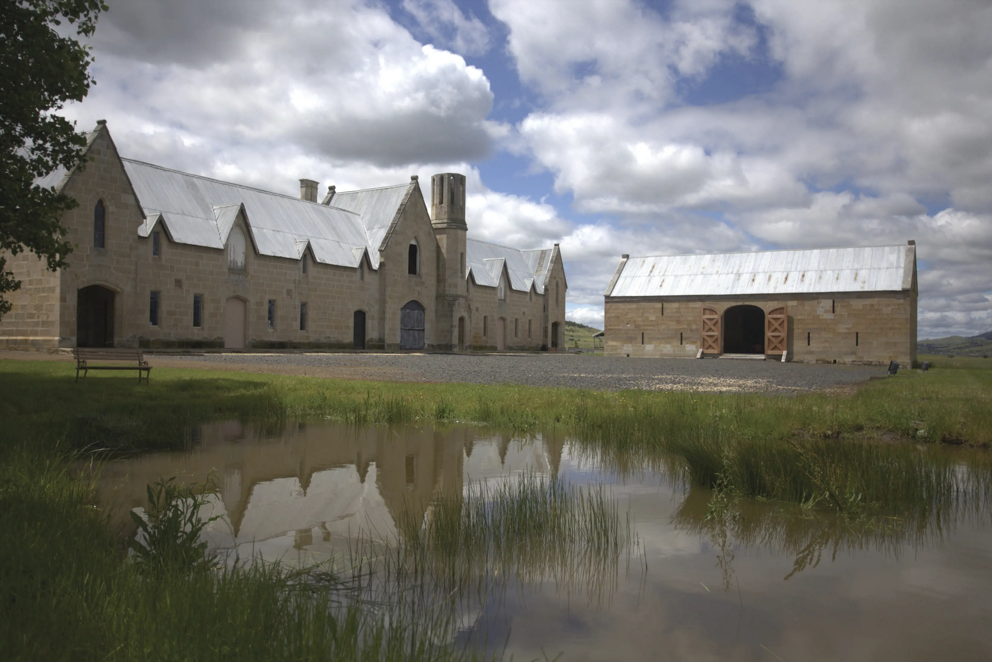 Lark Distillery from outside amongst lush greenery and calm water in the foreground of image.