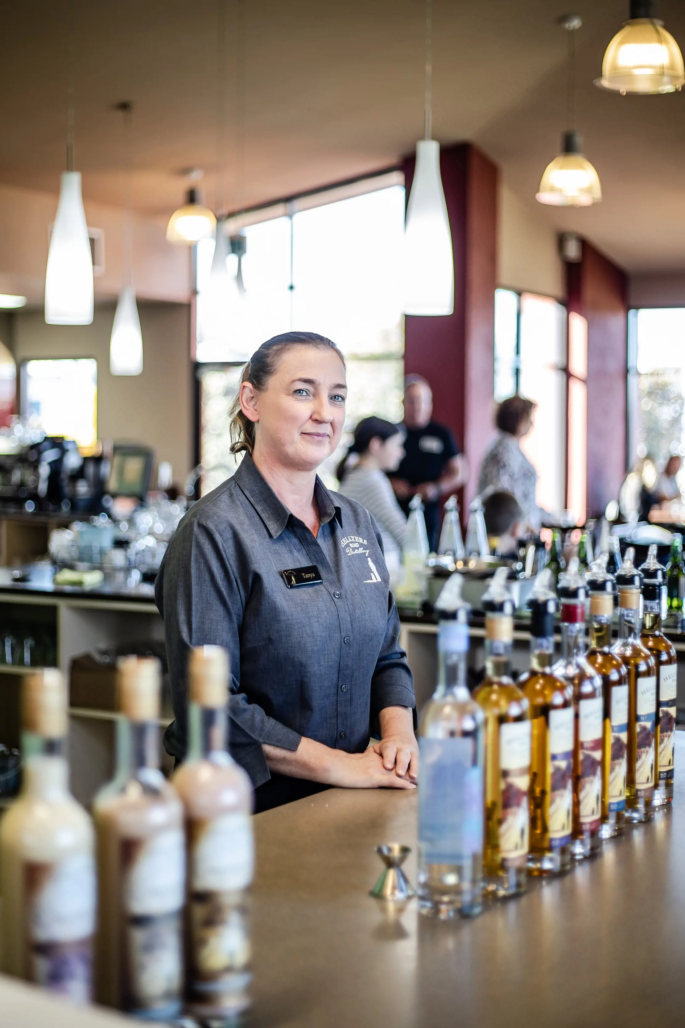 Lady behind the bar posing for photo with bottles of spirit placed in the foreground, on the bar table.