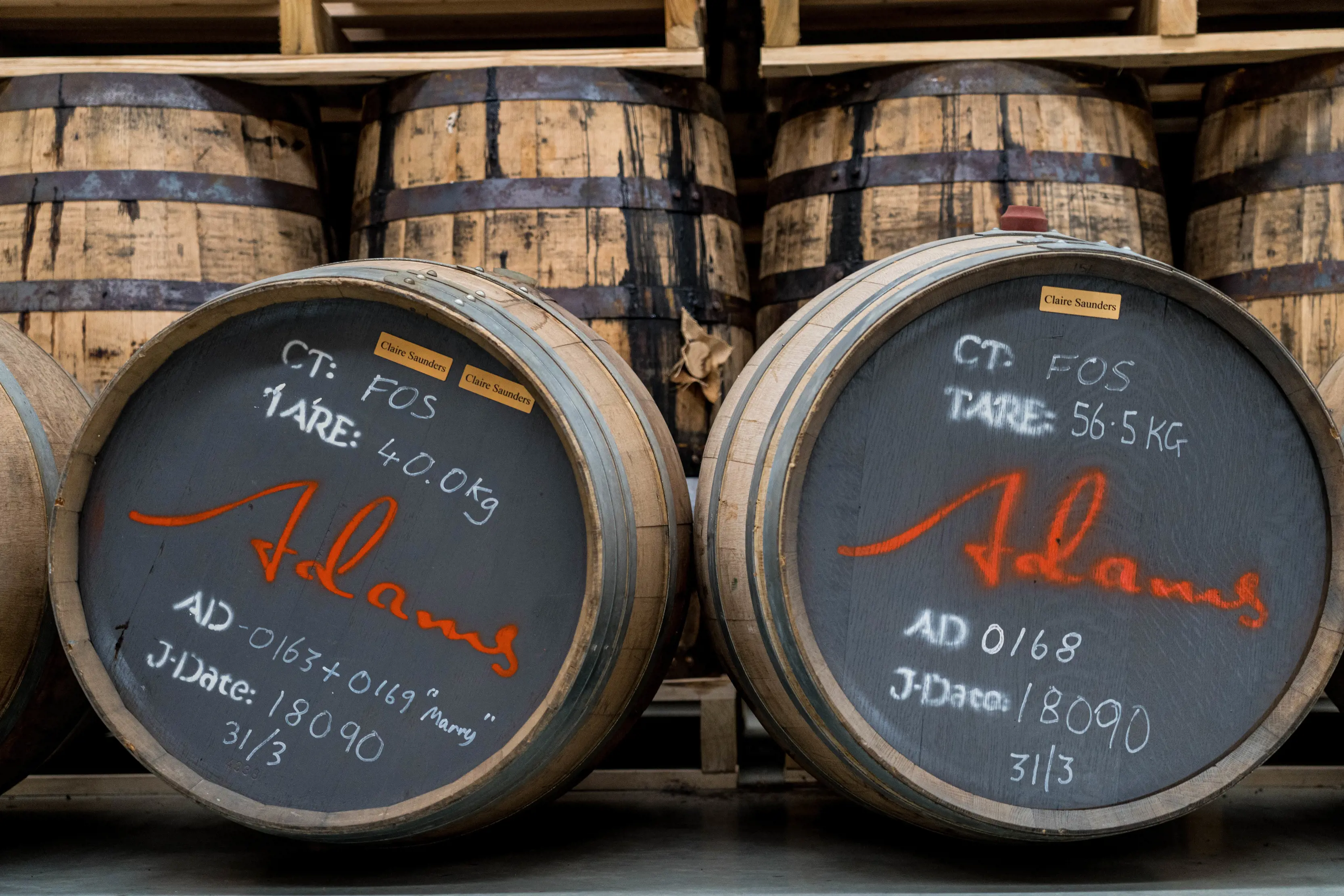 Two whisky barrels in the centre of the image with a stack of barrels in the background for Adams Distillery