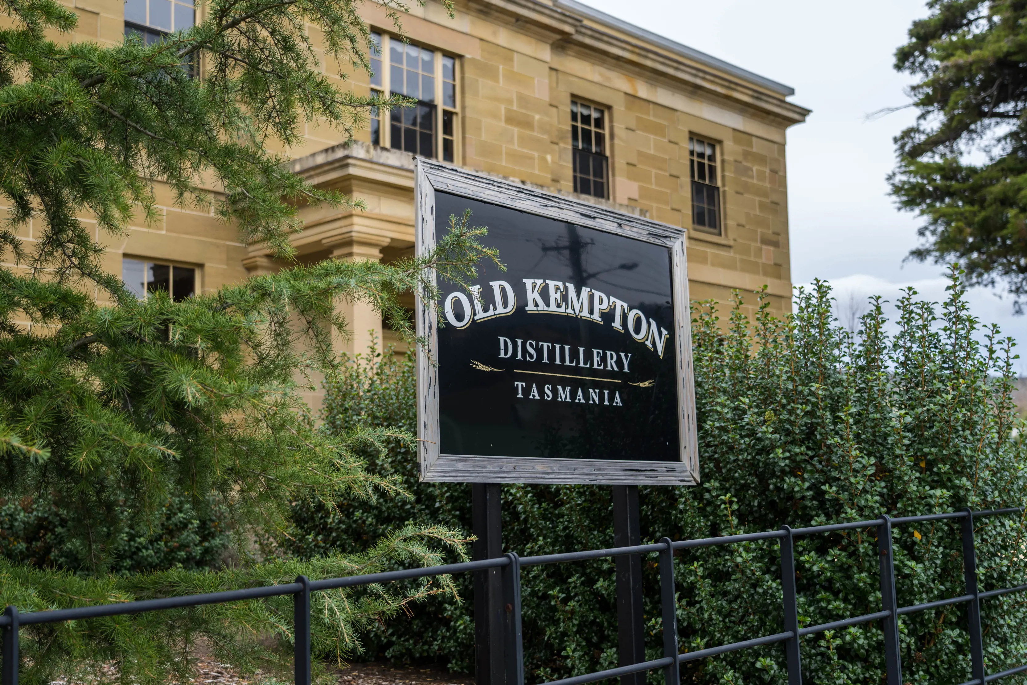 Image of the sign and outside the Old Kempton Distillery, located in Dysart House. Lush green trees surround the building.