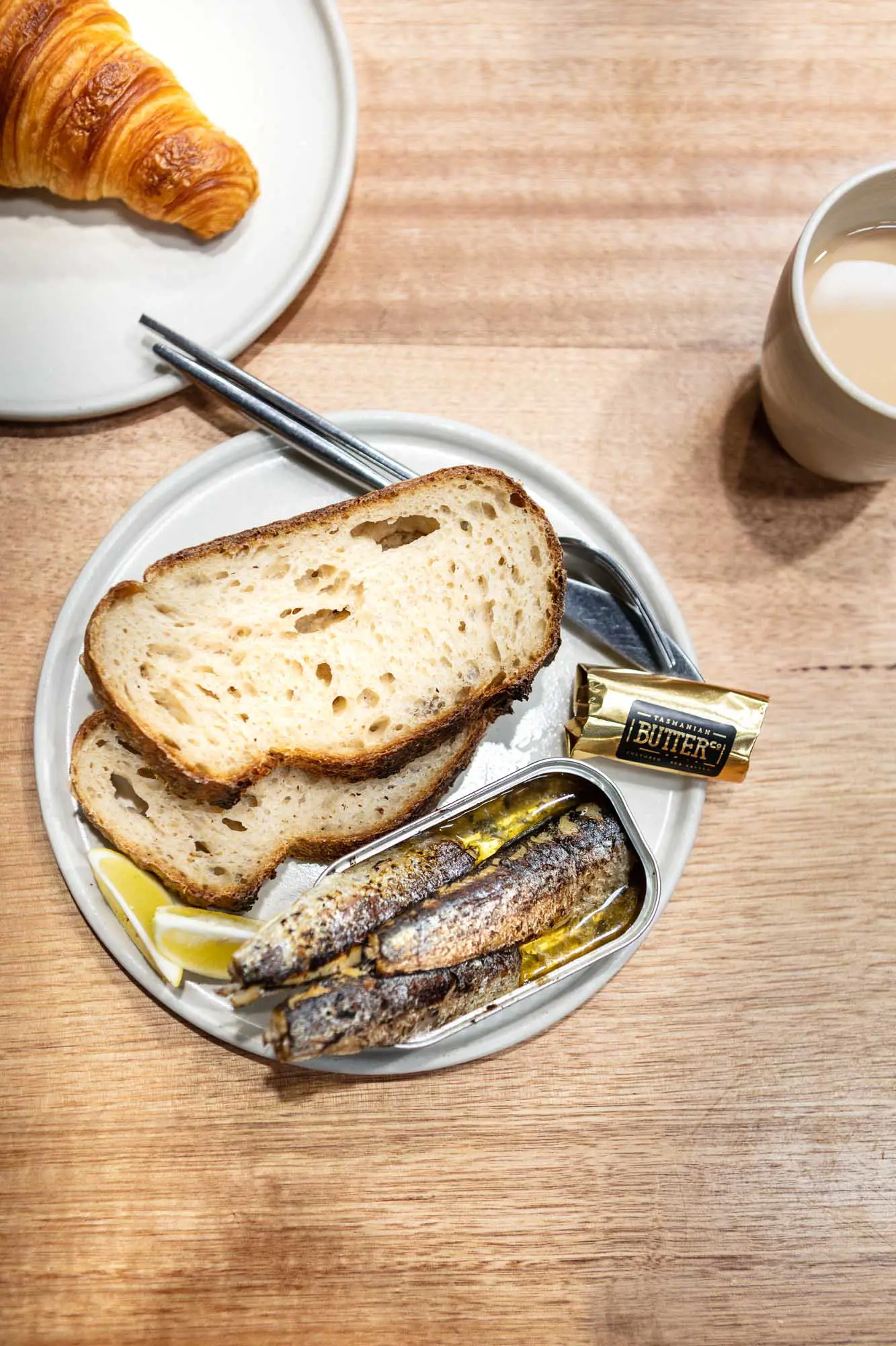 Bread and a tin of sardines with butter, placed on a white plate set on a wooden table.