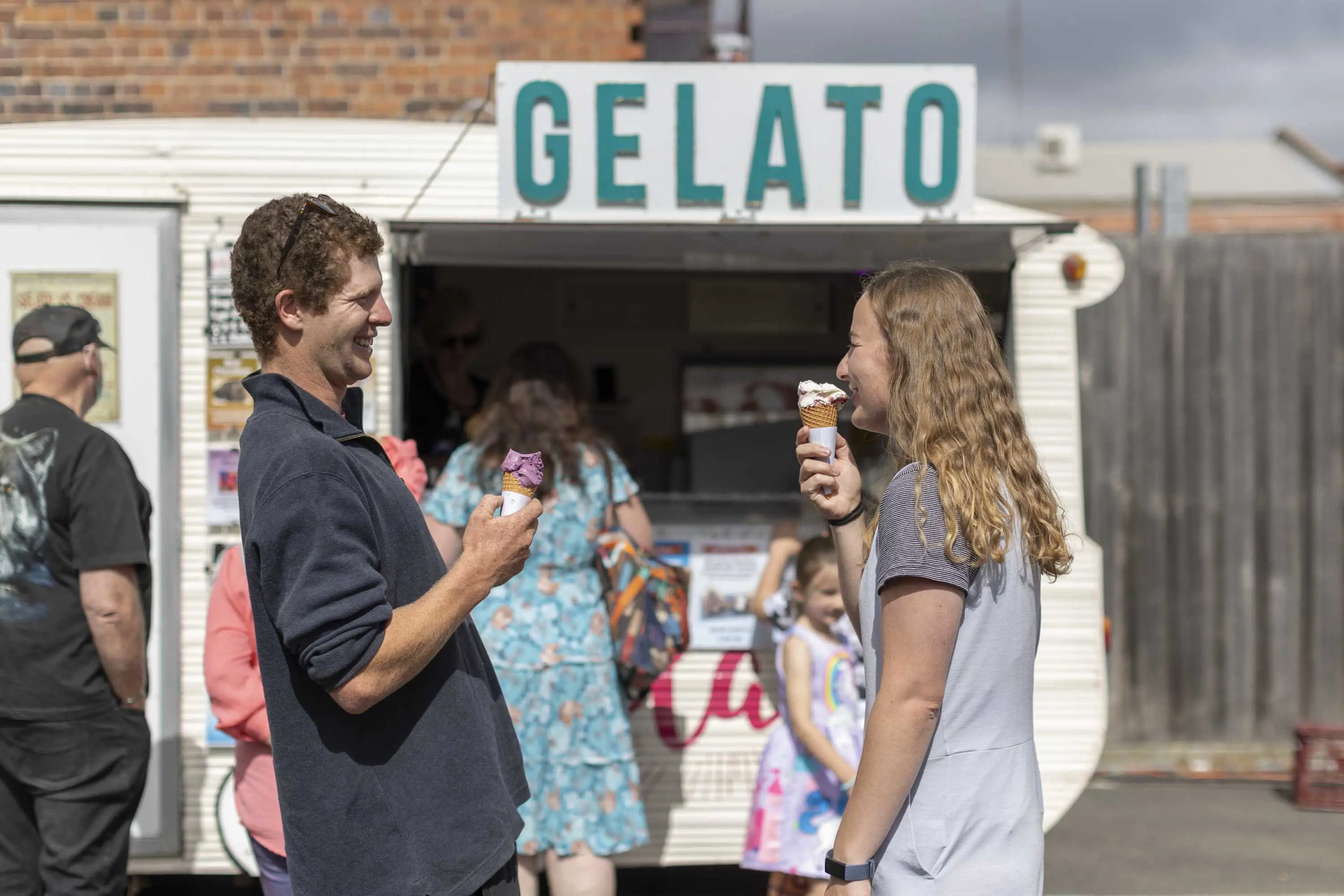 A young couple stand in front of a caravan that has been converted into a Gelato stand.