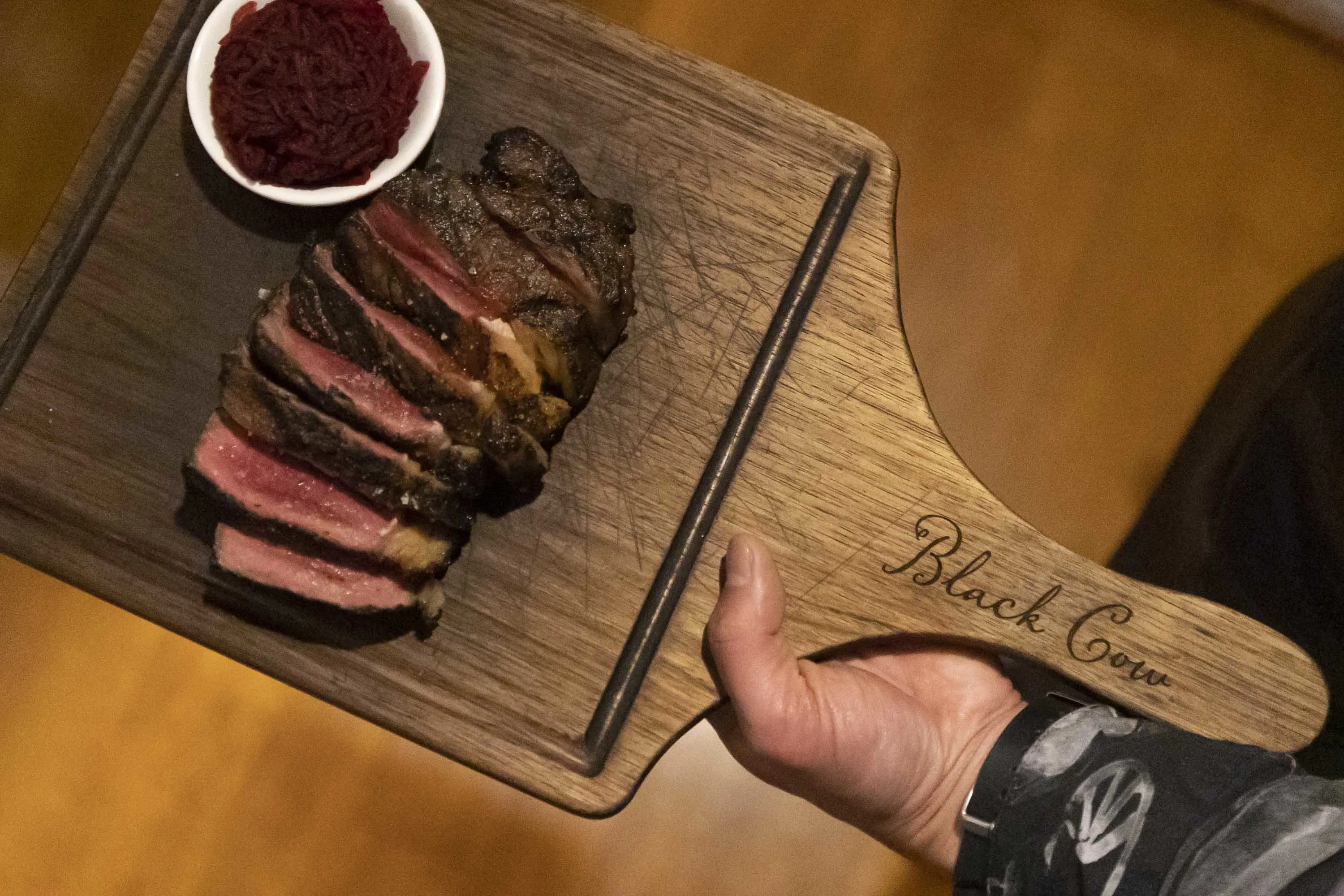A waiter holds a wooden board with beef, cooked medium-rare and thinly sliced. 