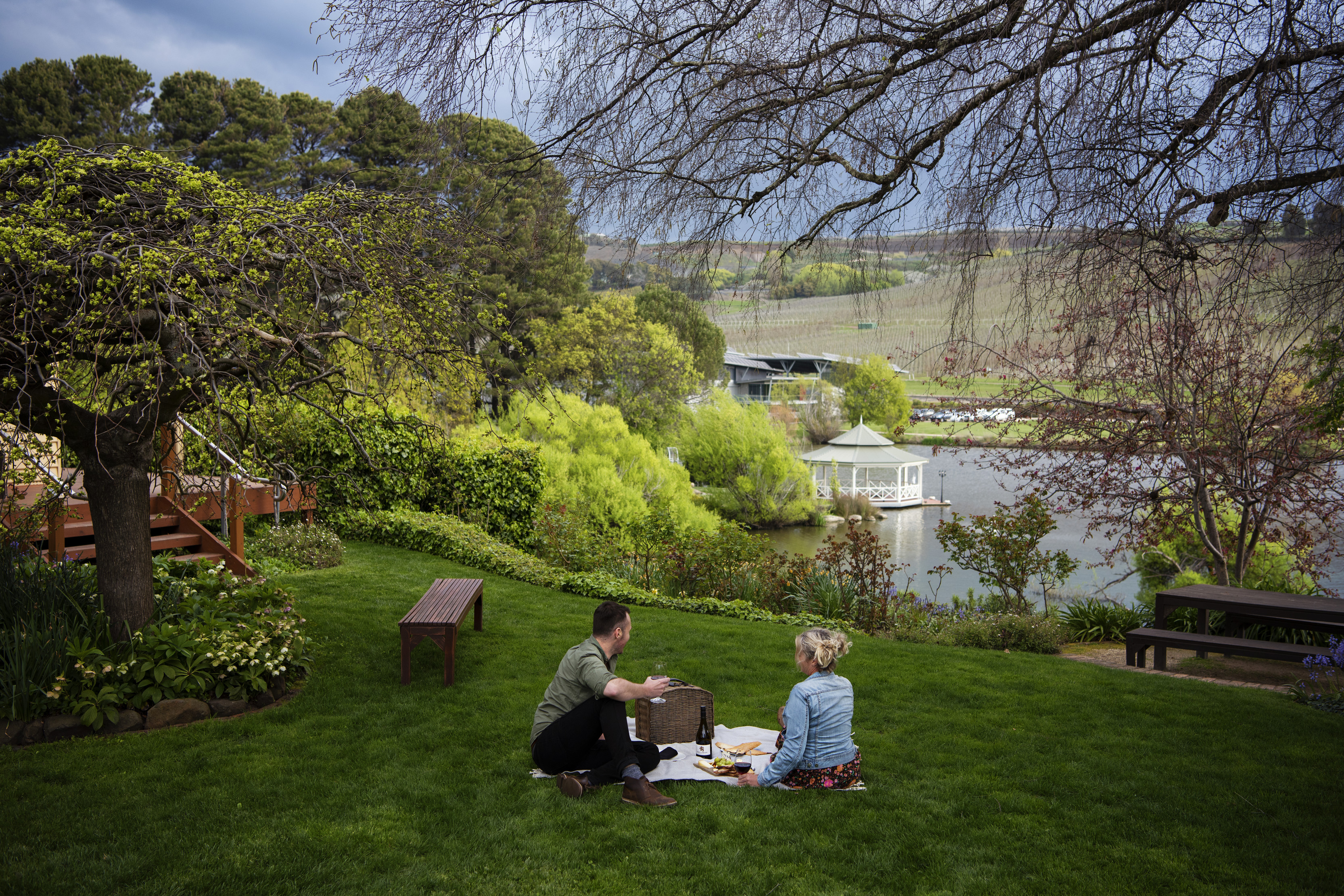 Couple having picnic under a tree amongst the lush, greenery at Picnic at Josef Chromy Tasmania.
