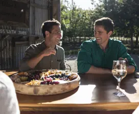Two friends enjoy a platter of cheese and fruit at a long wooden table.