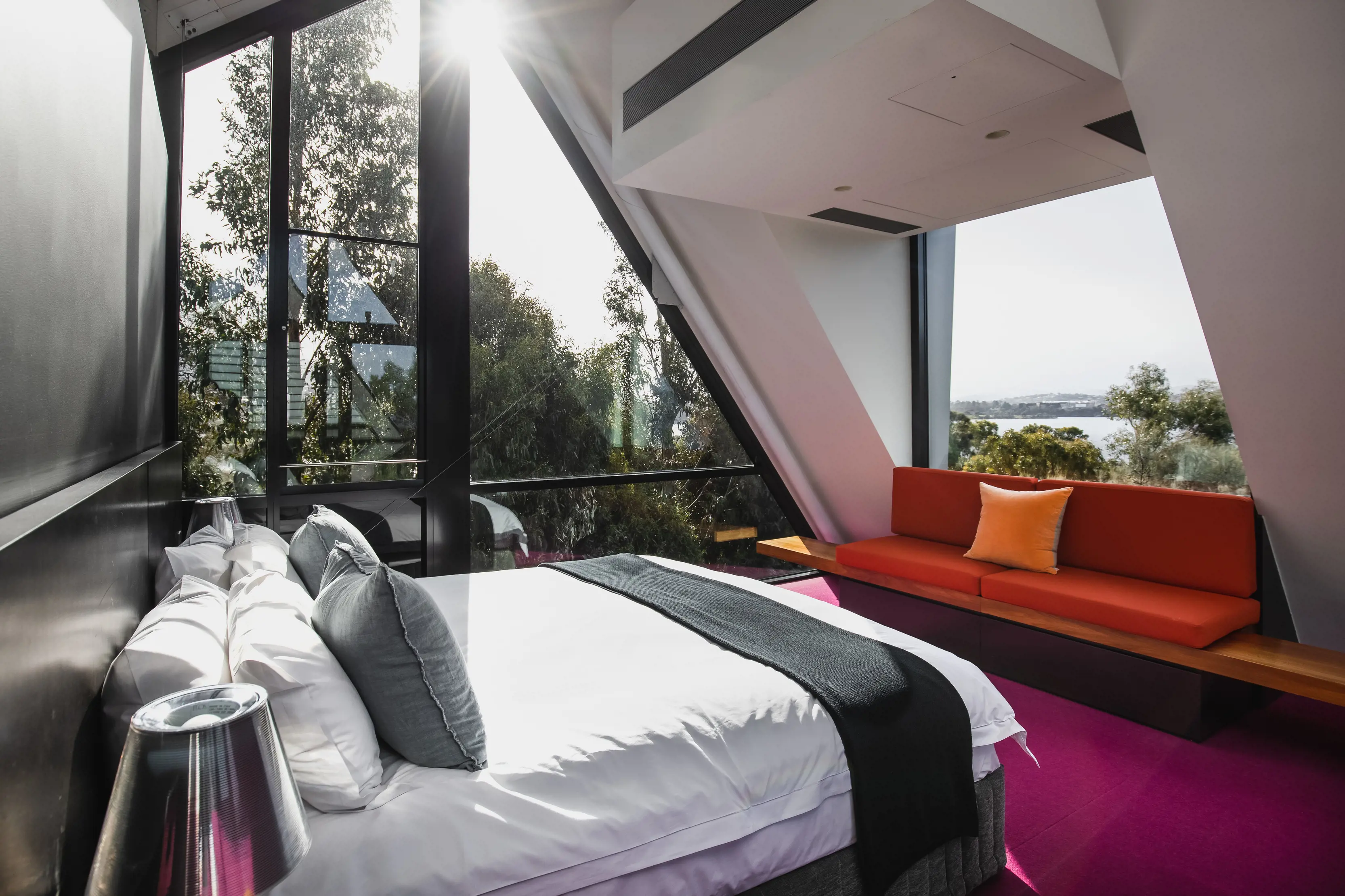 Interior of a bedroom with a bed, orange sofa and water views at Walter Pavilion, MONA Pavilions.