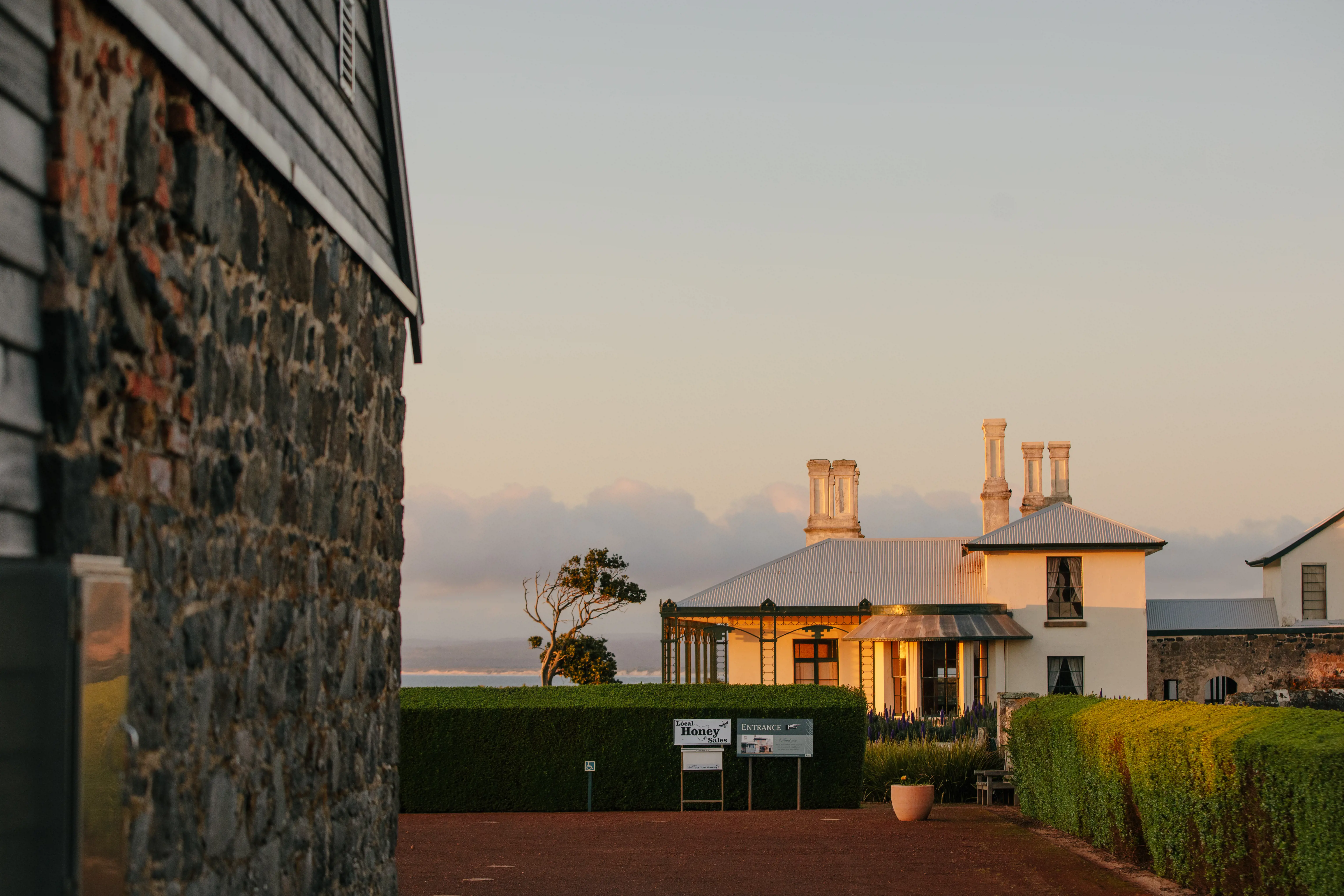 In the light of the setting sun, an elegant white-rendered historic cottage sits amongst manicured hedges.