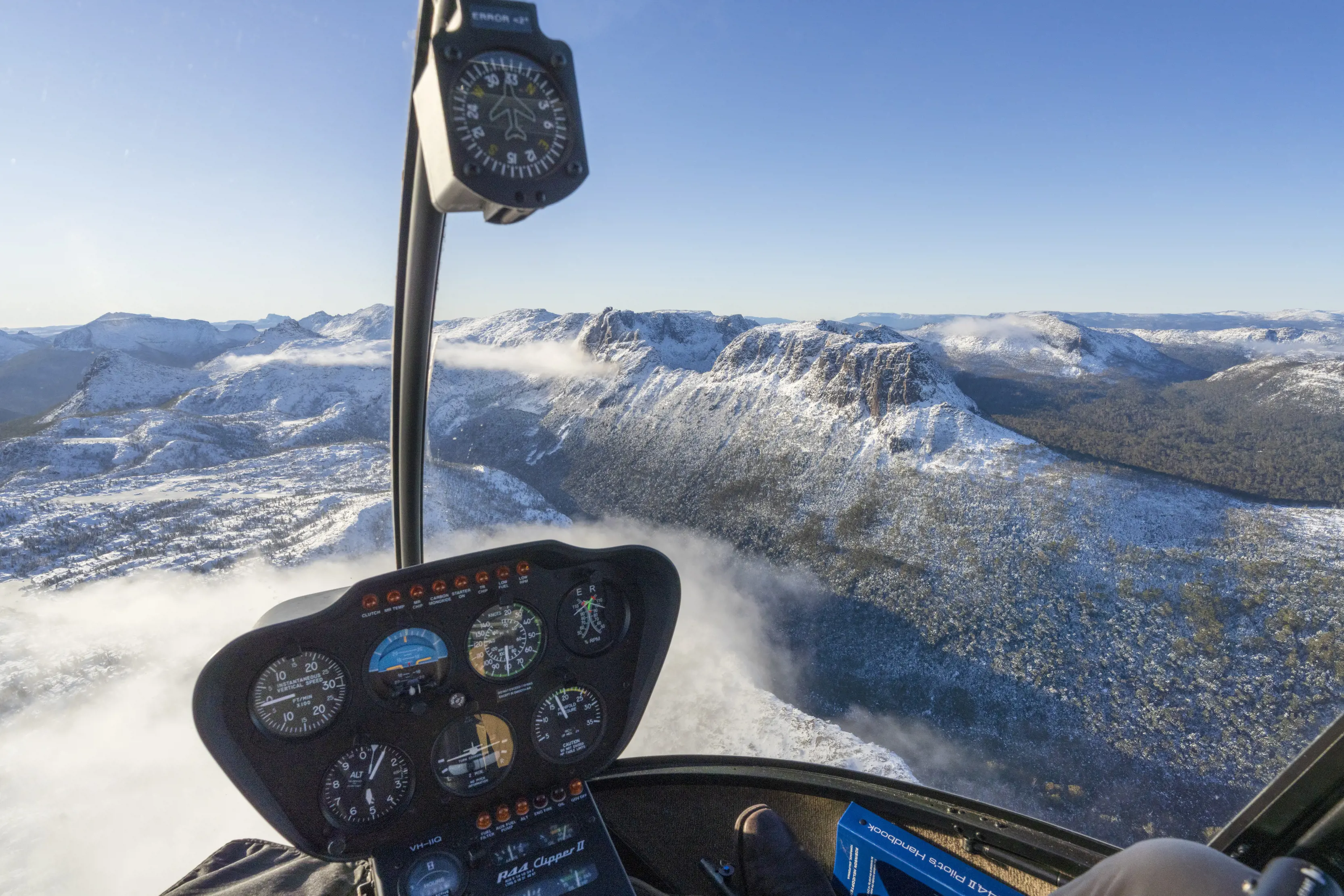 Breathtaking point of view image taken from a helicopter by Tasmanian Air tours of the mountains and surrounding nature, which is covered in snow.