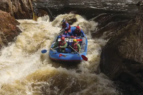 Intense image of four people white water rafting in rough waters on the Franklin River.