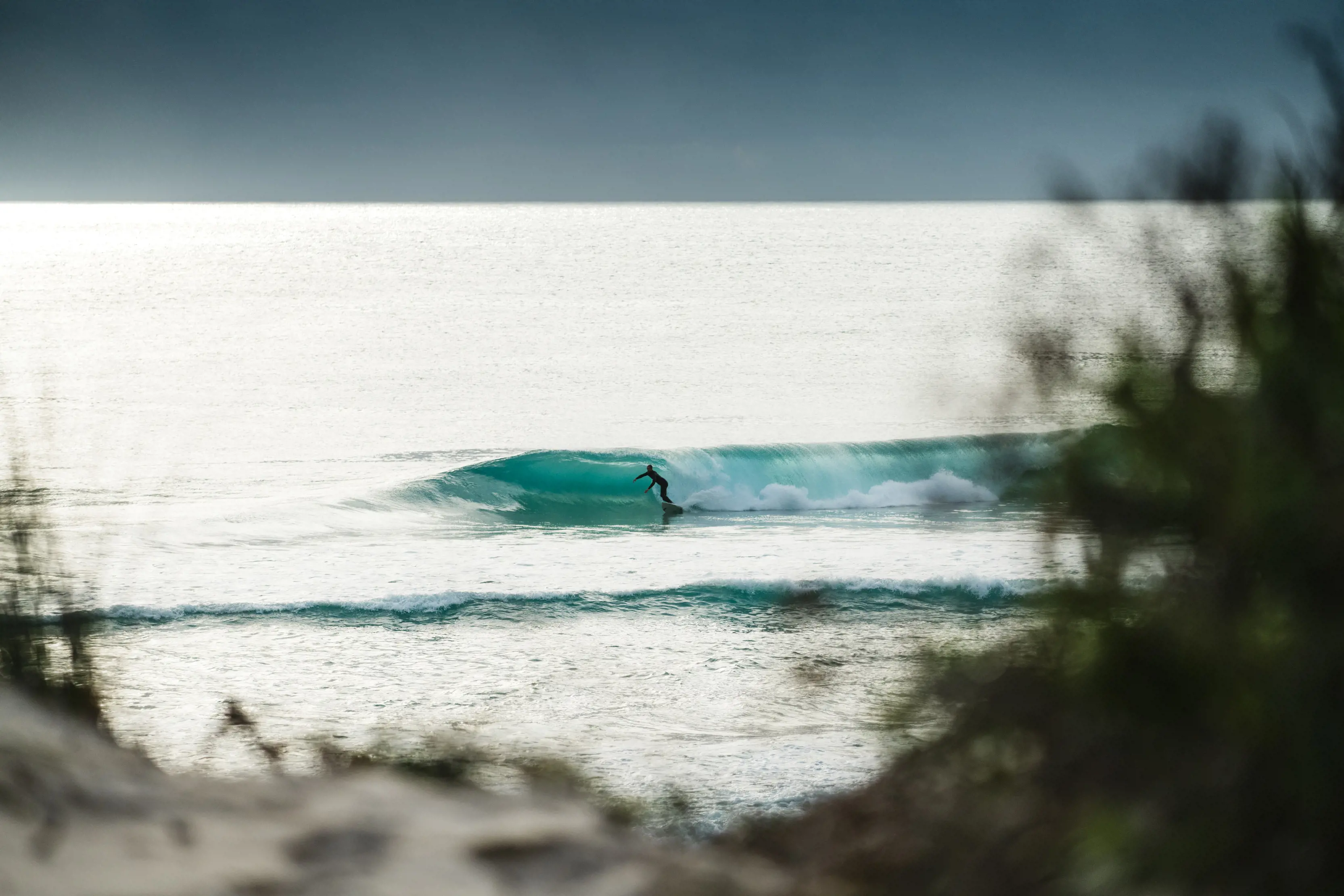 Stunning image taken from land of a surfer inside a crystal blue, hollow wave. 