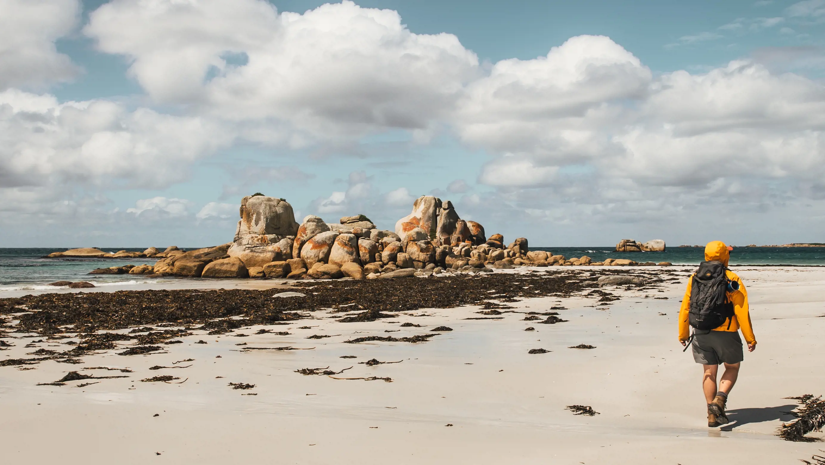 Man walking along shoreline of a beach with incredible rock formations that fill the centre of the image, on the Wukalina Walk.